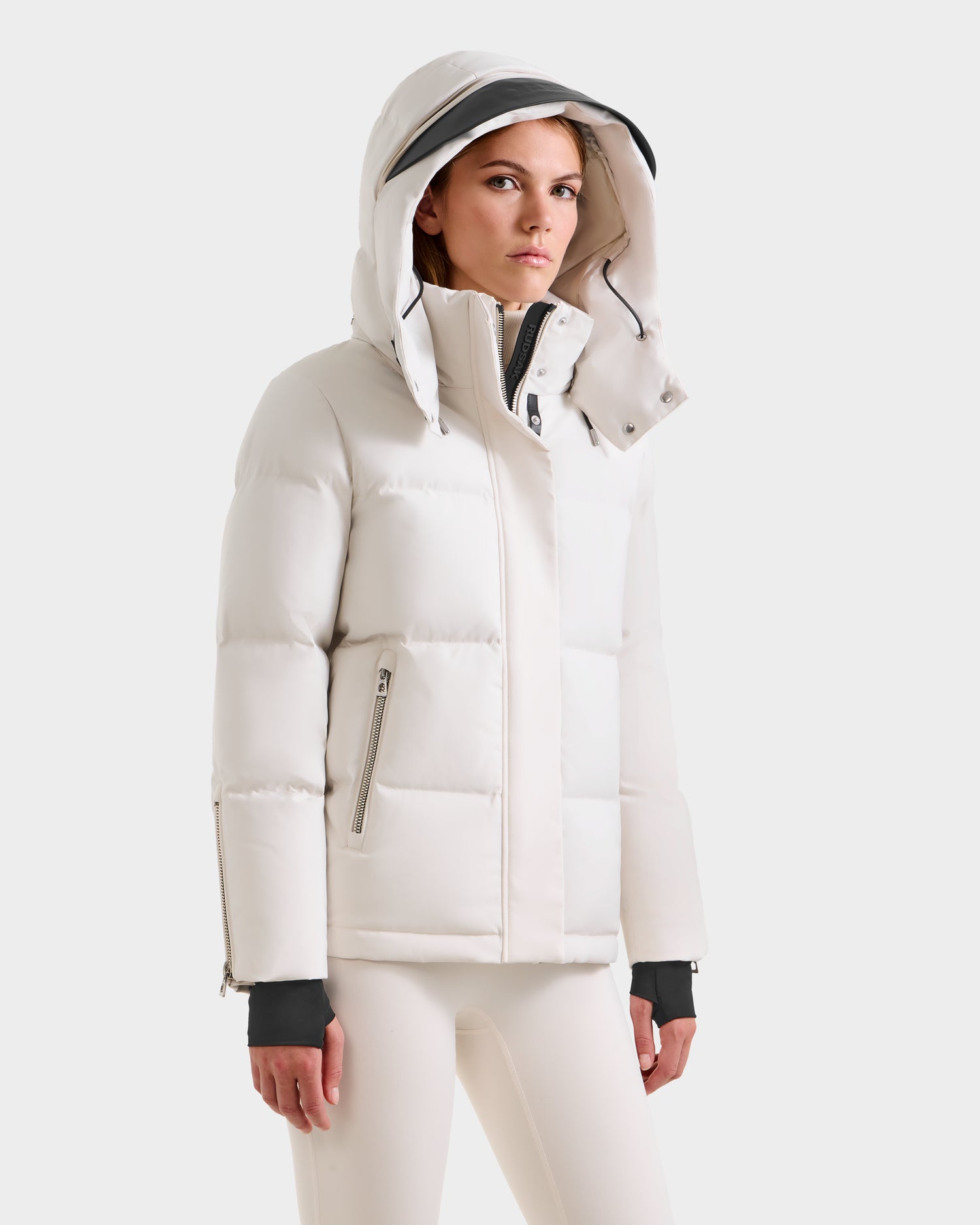 A woman wears the Rudsak JOON H - 8125586 Vanilla quilted winter jacket with a hood and zippered pockets, paired with matching white pants, standing against a light background and looking slightly to the side.