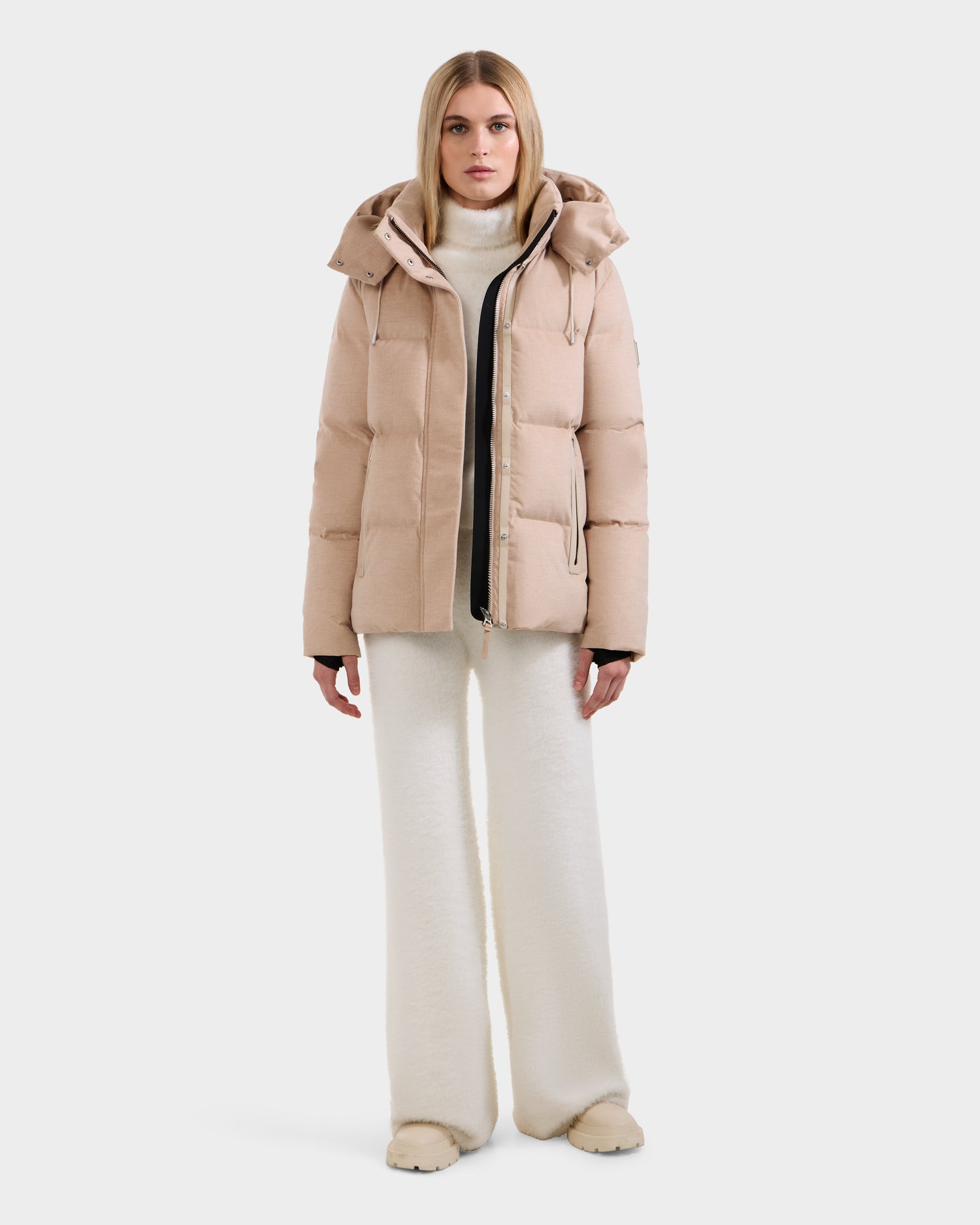 A woman faces forward in the Rudsak JOON W - 8125566 Heather Beige wool-blend down puffer jacket with hood, layered over a white turtleneck and wide-leg pants, plus beige shoes, all set against a plain white background.