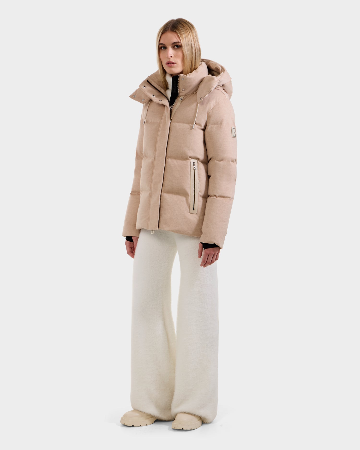 A woman wearing the Rudsak JOON W - 8125566 Heather Beige wool-blend down puffer jacket with a hood, off-white wide-leg pants, and matching shoes stands against a plain white background.