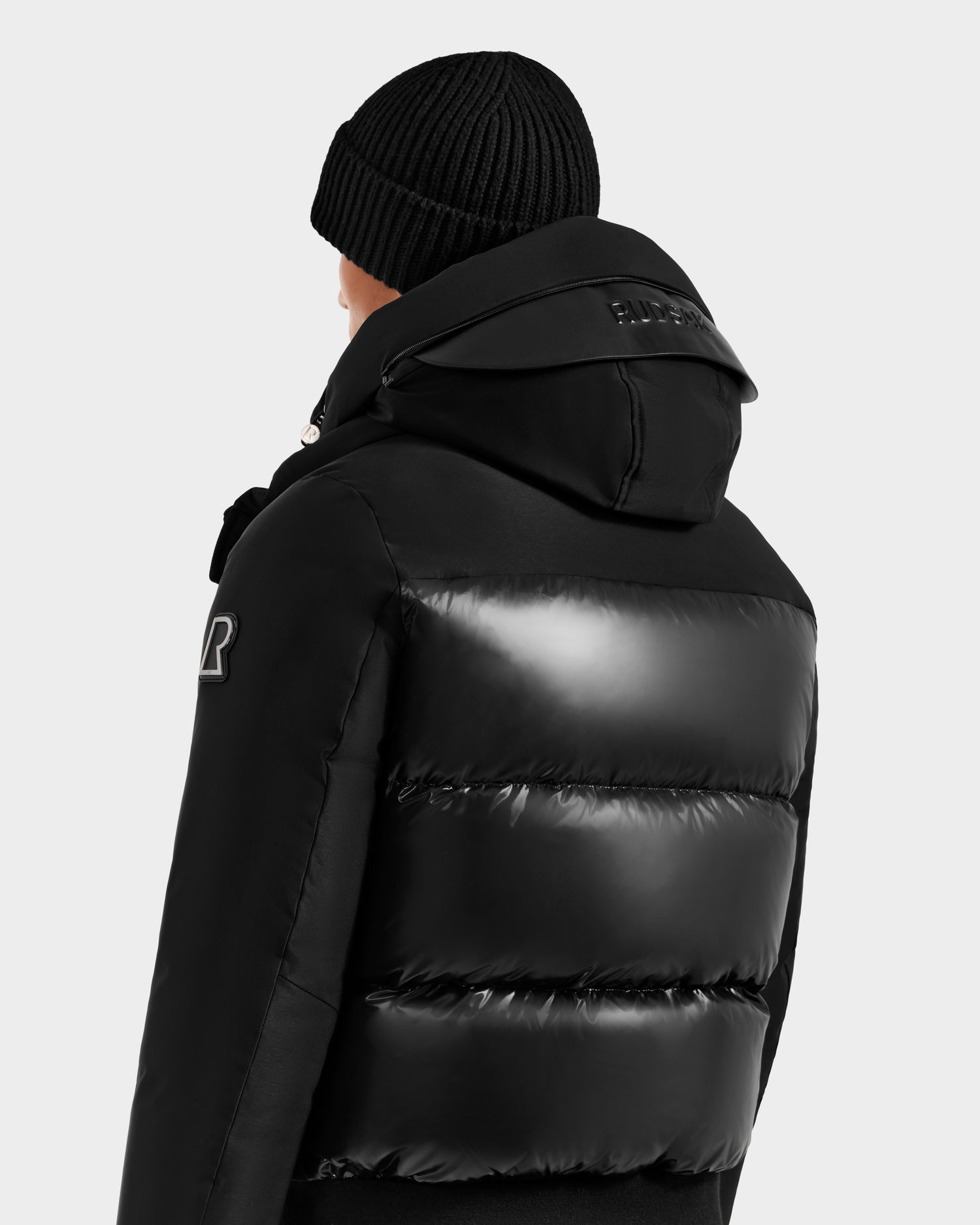 A person is seen from the back against a light background, wearing the Rudsak JORDY H - 6125689 Black men's quilted down bomber with a hood and a black knit beanie, highlighting winter warmth and modern style.