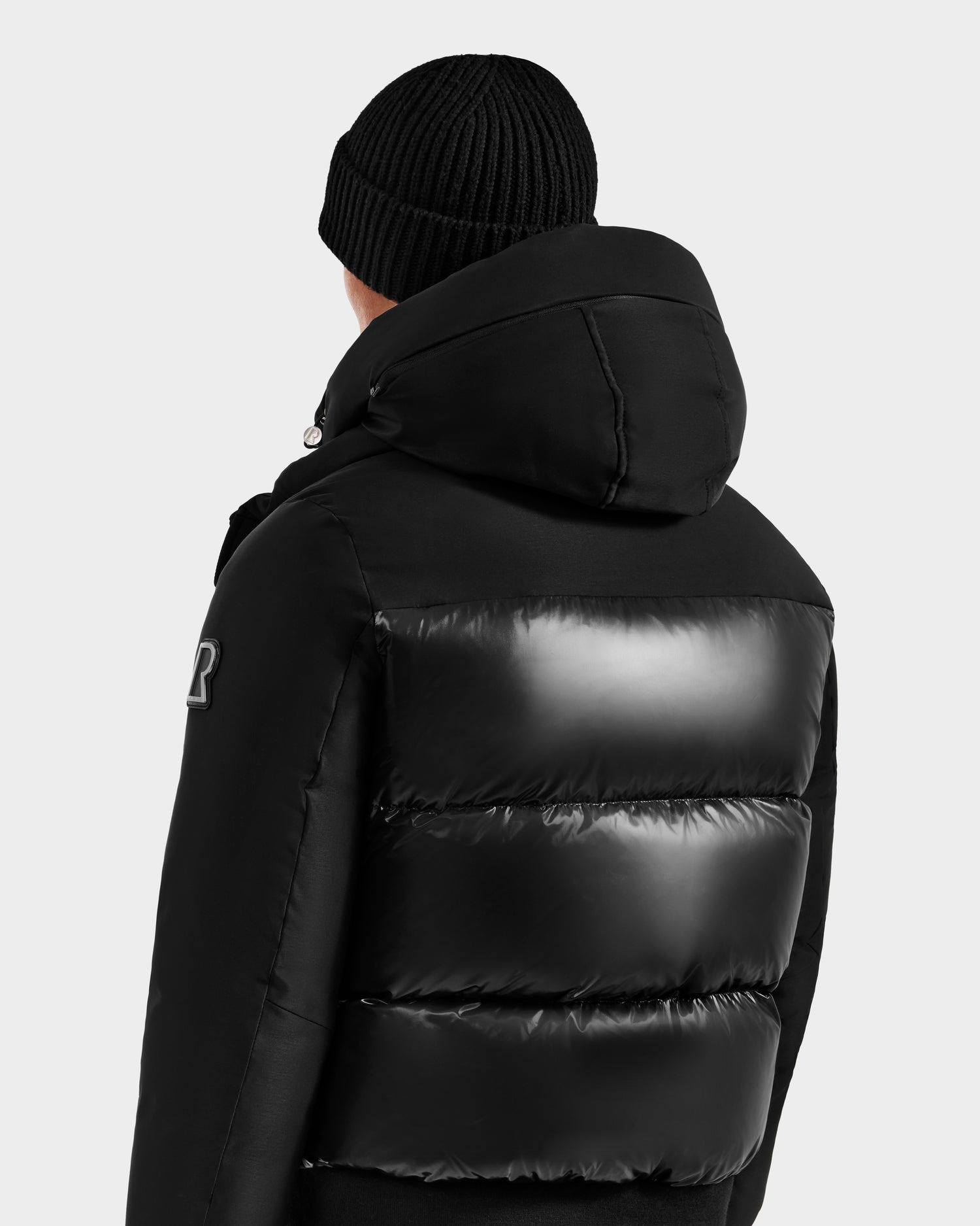 A person is shown from the back wearing the Rudsak JORDY H - 6125689 Black quilted down bomber with hood against a plain light gray background, emphasizing its cozy winter warmth.