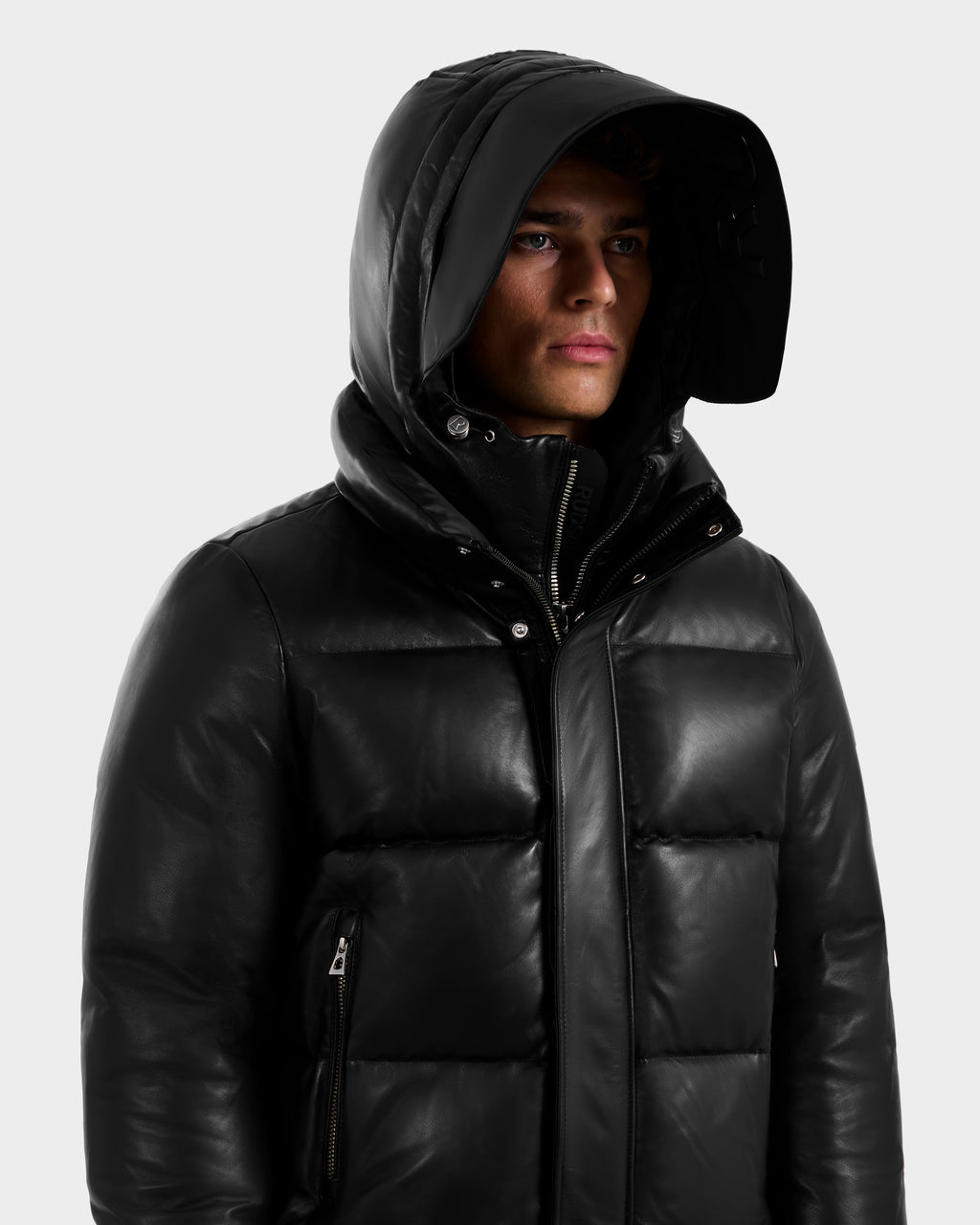 A person wears the Rudsak JORDY X - 6125694 Black quilted bomber jacket with the hood up, looking slightly to the side against a plain light background.