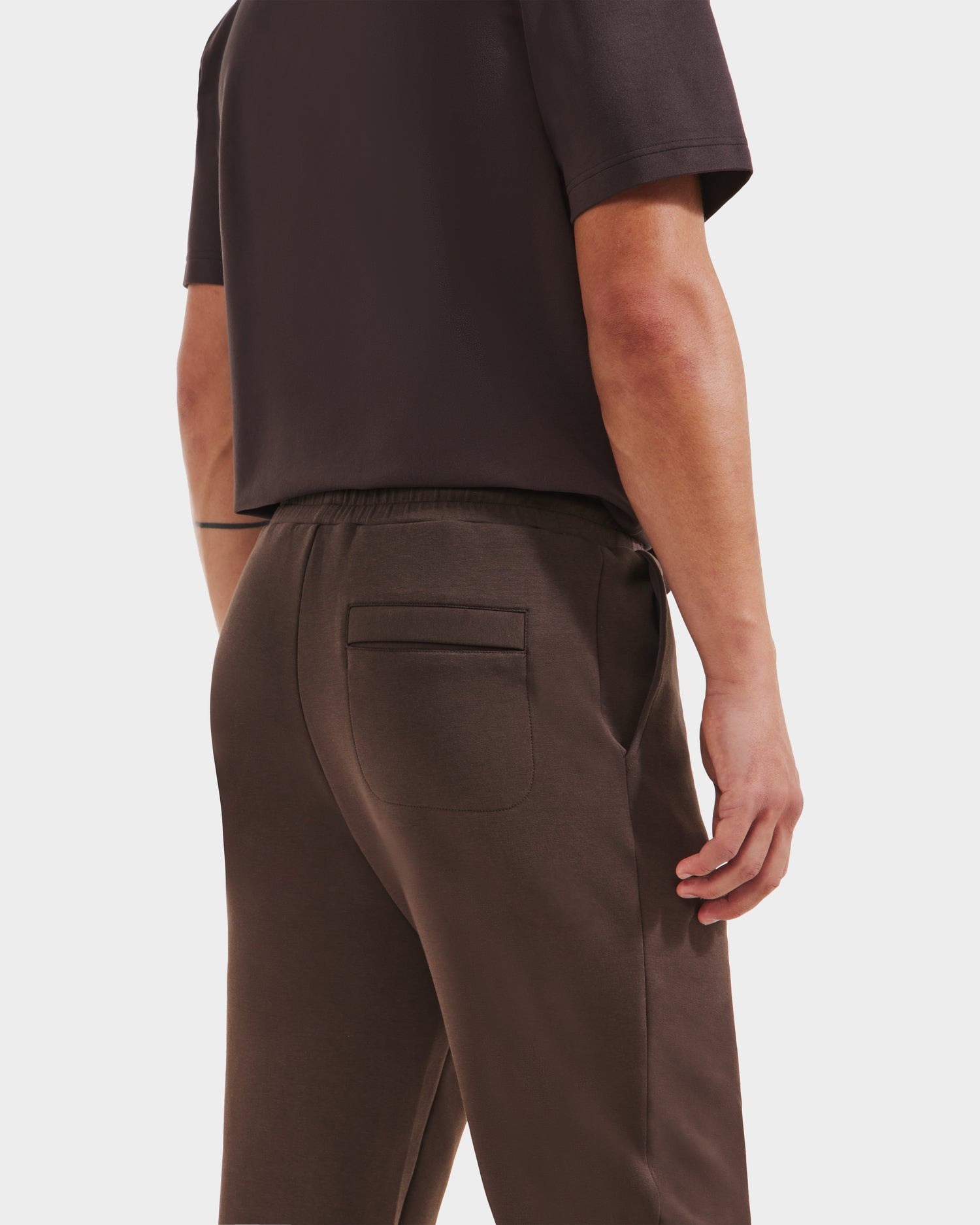 A person is shown from the back wearing a Rudsak JOSS - 9524009 Espresso M short-sleeve shirt and modern jogger pants with a back pocket and elastic waistband for comfort, one hand resting at their side.