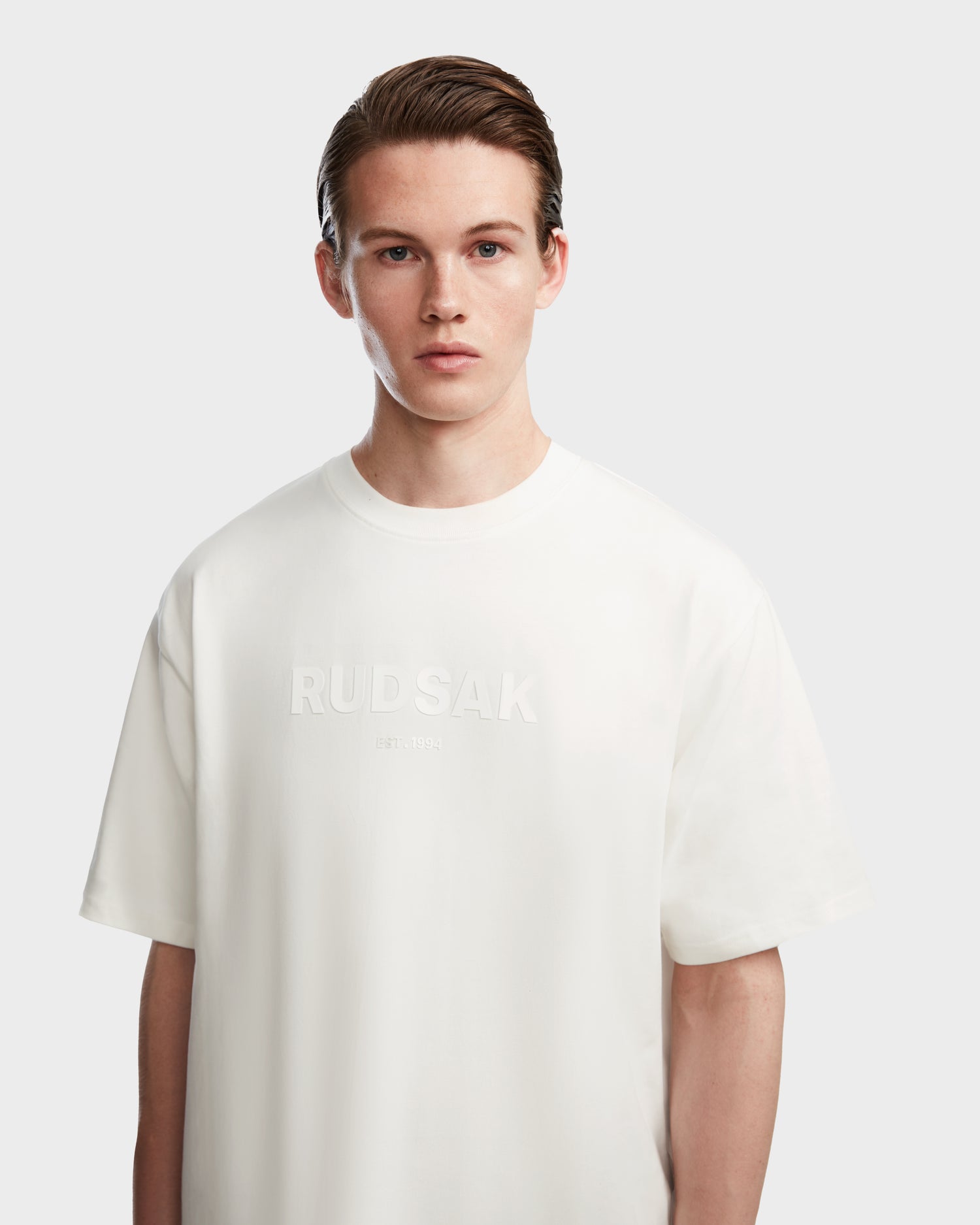 A young person with light skin and short, neatly combed brown hair wears the Rudsak KARTER - 9524008 Iceland M premium cotton T-shirt, standing against a plain light gray background.