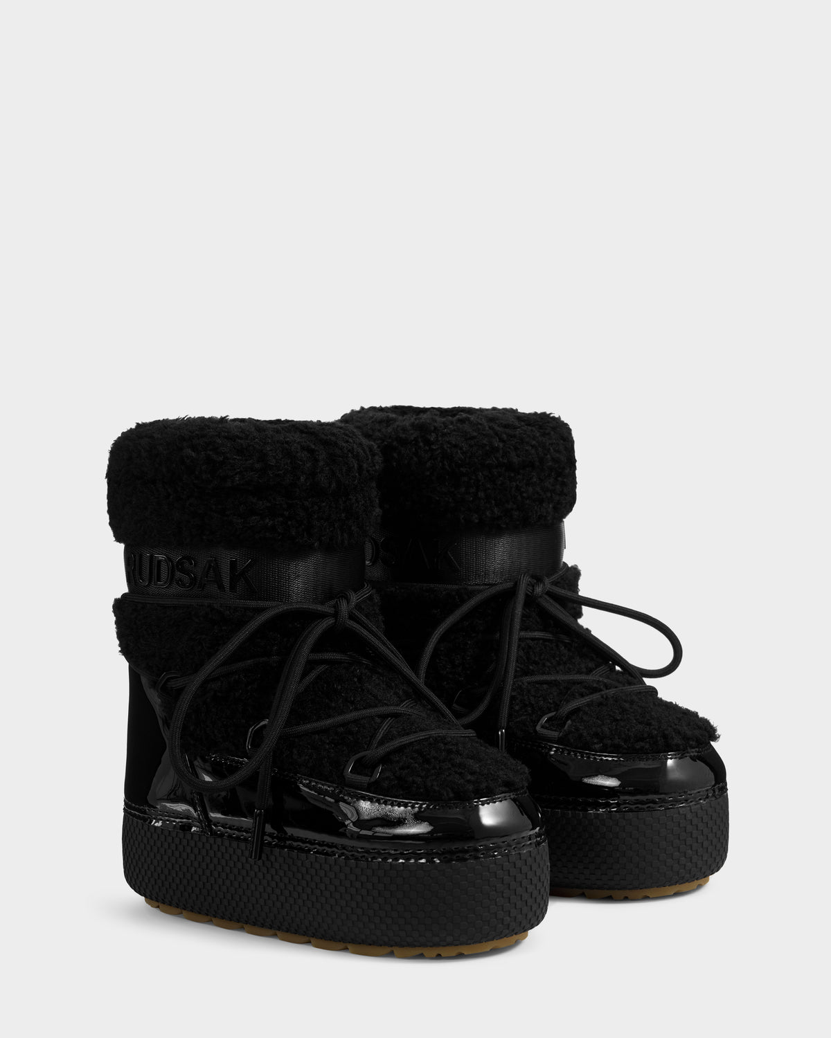 The Rudsak KATHY Y - 1224500 Black boots feature water-repellent shearling uppers, glossy patent leather accents, thick textured soles, black laces, and an insulated look for cozy winter wear.