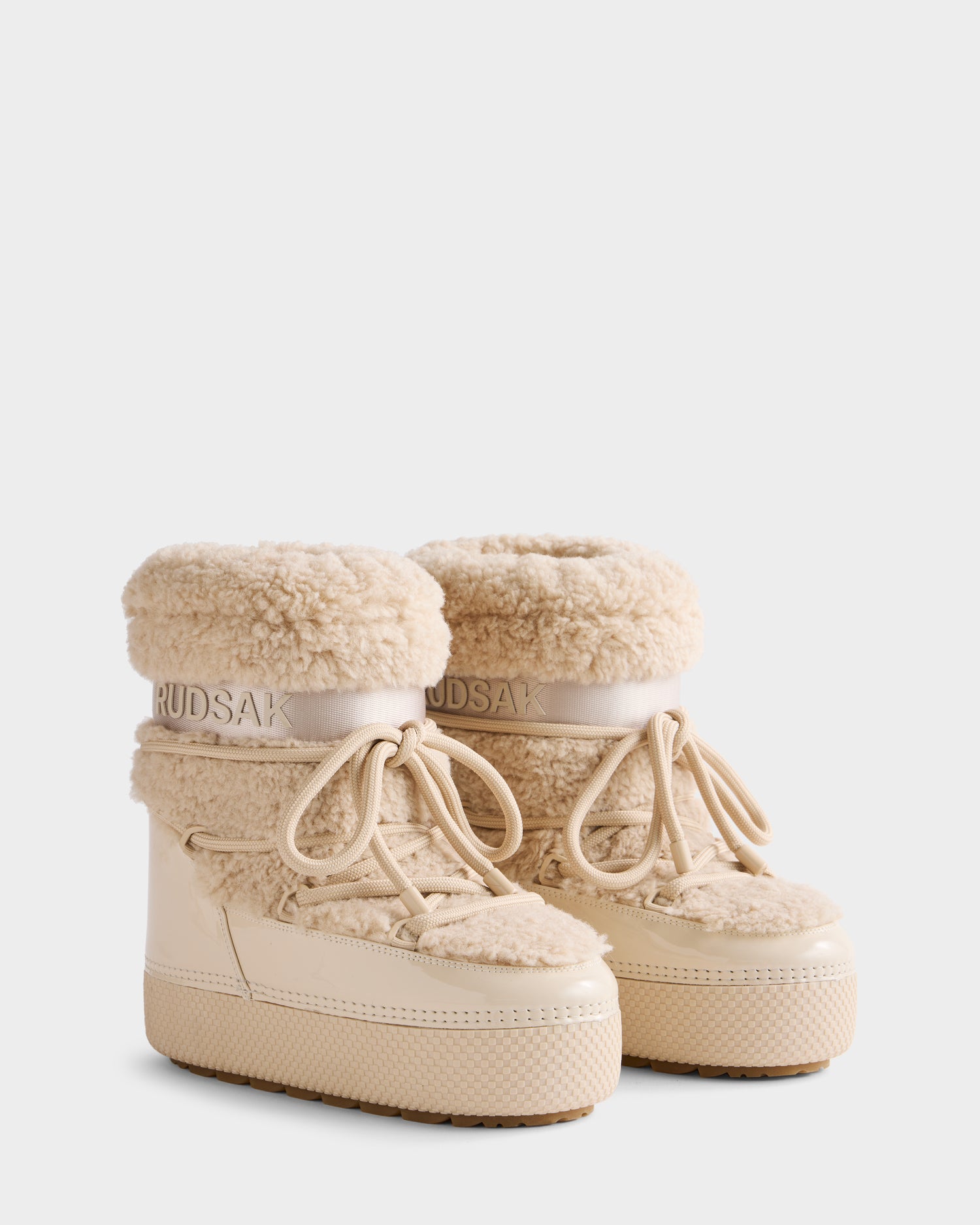 The Rudsak KATHY - 8223513 Vanilla women's winter boots feature a beige design with thick textured soles, faux shearling lining, glossy lower section, water-repellent finish, laces, and Rudsak branding on the cuff.