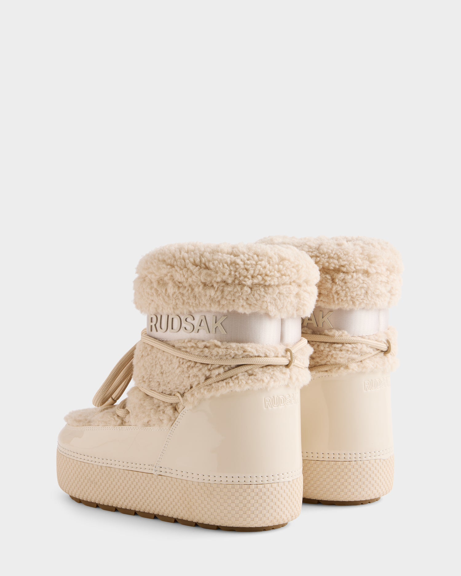 The Rudsak KATHY - 8223513 Vanilla women’s winter boots feature beige patent leather, plush sherpa trim, thick soles, water-repellent design, and branding on the back—shown from behind on a white background.