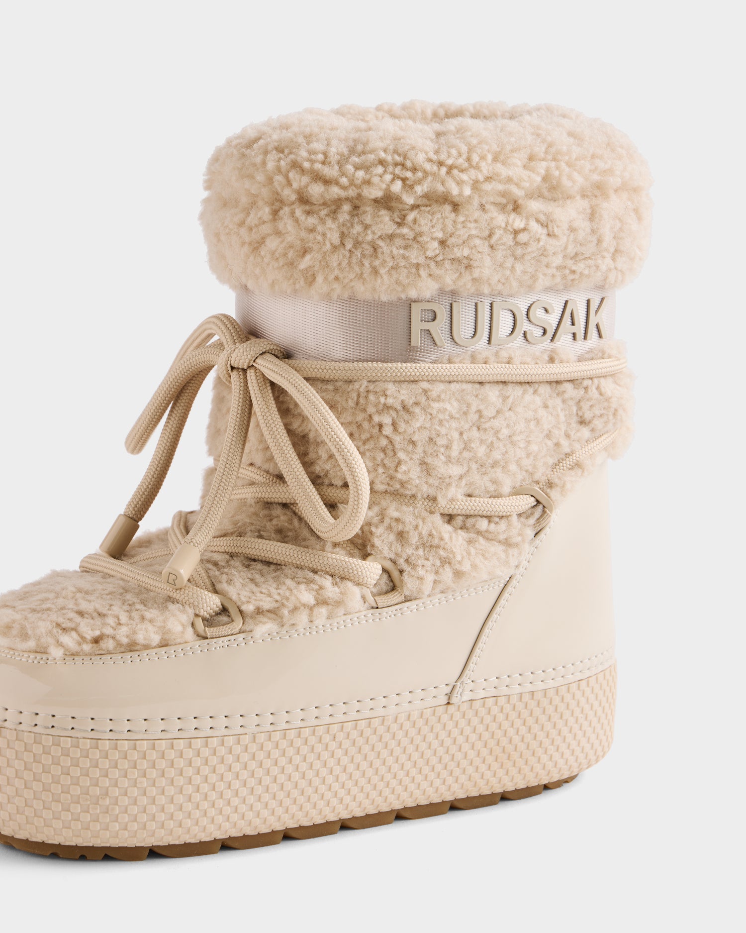 The KATHY - 8223513 Vanilla by Rudsak is a beige faux shearling women’s winter boot featuring a thick sole, lace-up front, and Rudsak branding near the top—offering cozy style and warmth for cold days.