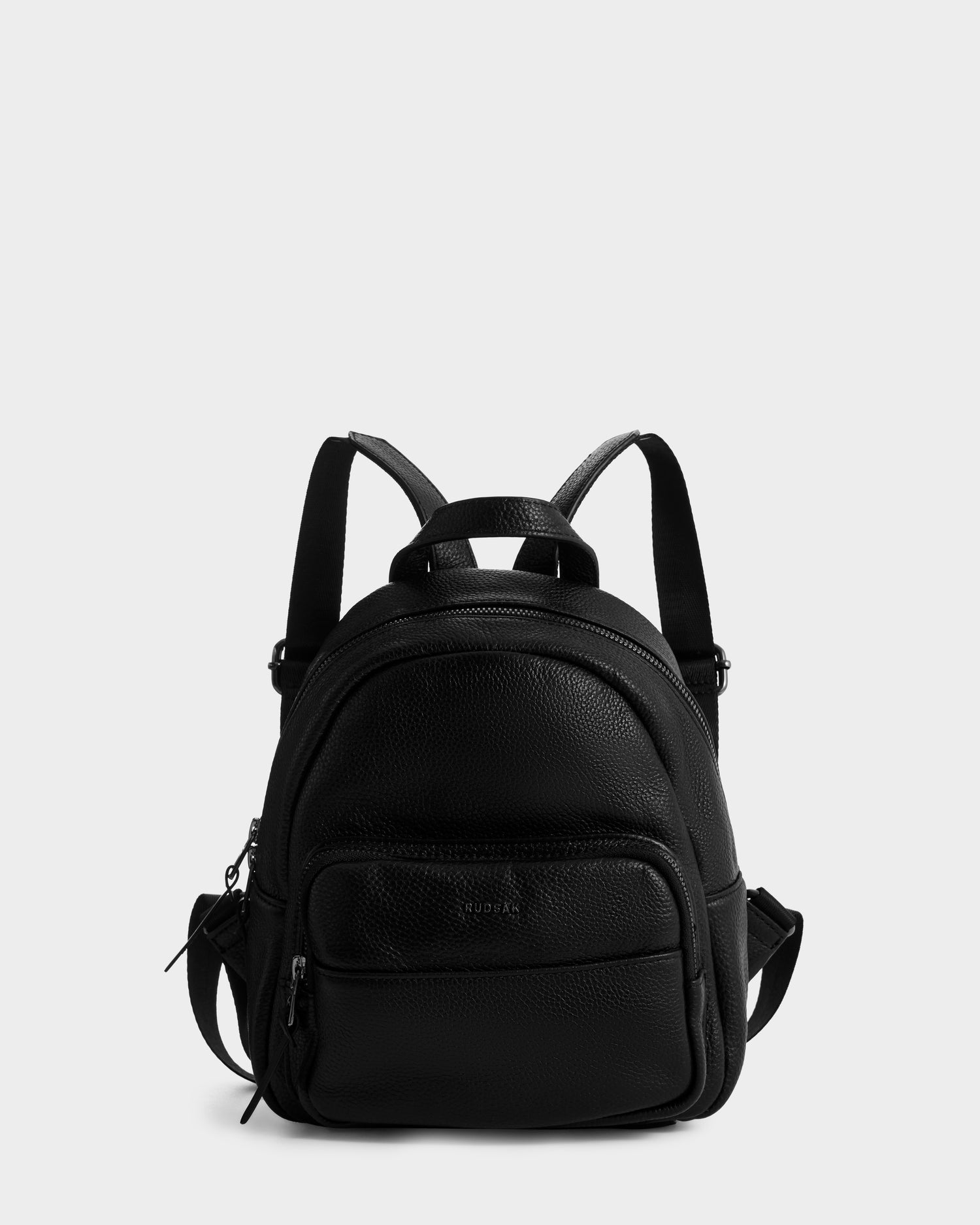 The Rudsak KATTY - L325014 Black is a small black pebbled leather backpack with two zippered compartments and adjustable shoulder straps, shown against a plain white background.