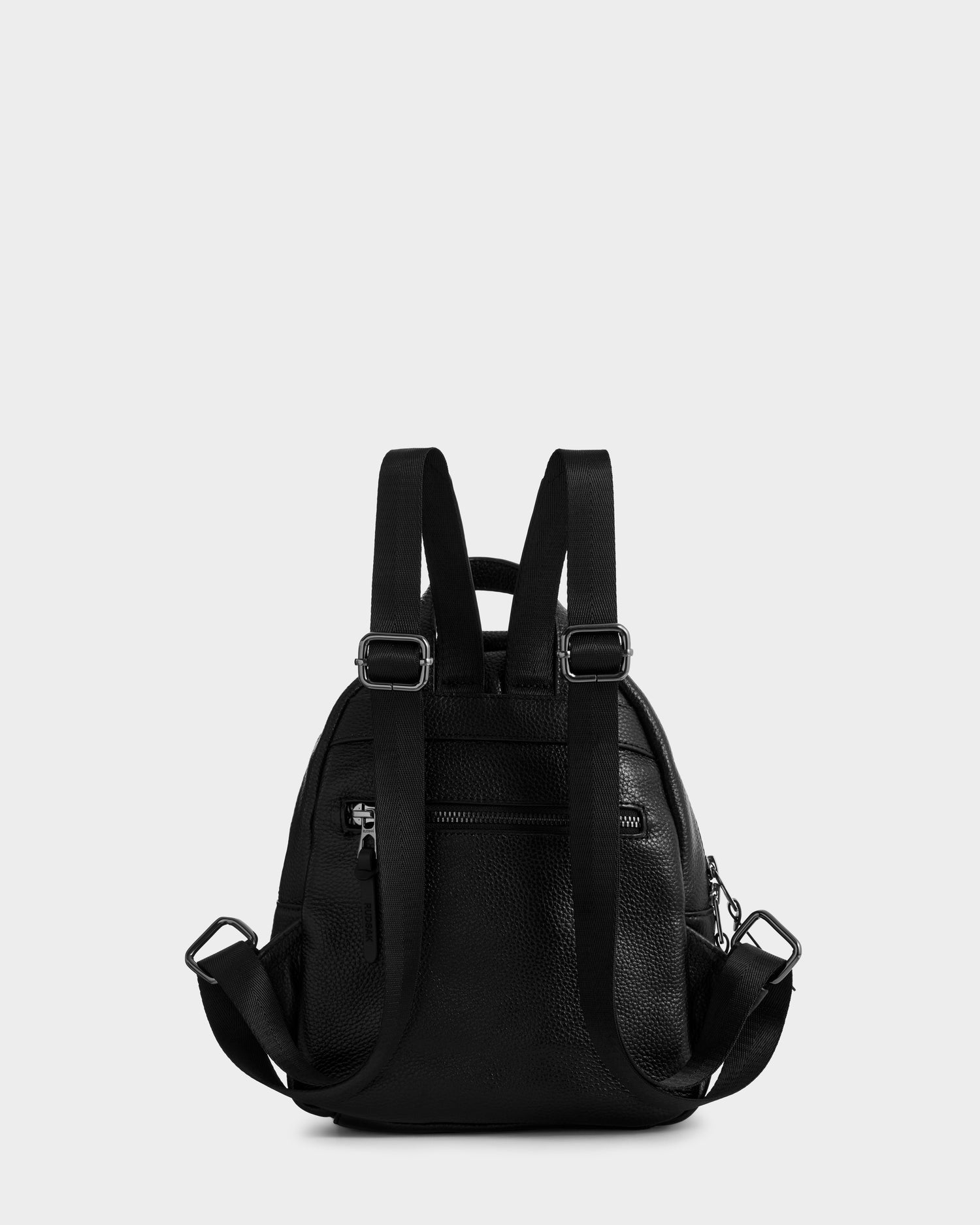 The Rudsak KATTY - L325014 Black backpack, crafted in black pebbled leather, is shown from the back with adjustable shoulder straps, a top handle, metal hardware, and a zippered back pocket against a plain light gray background.