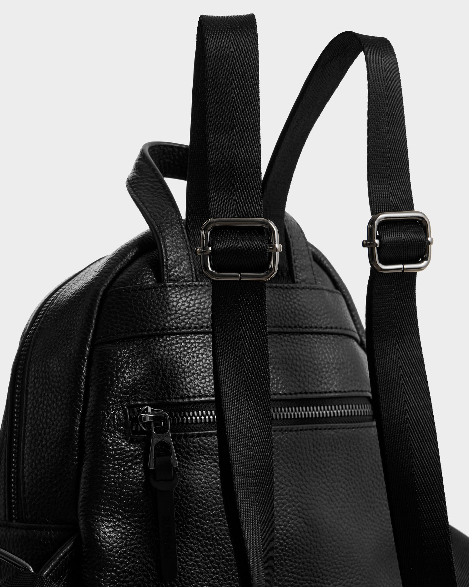 Close-up of the Rudsak KATTY - L325014 Black pebbled leather backpack with silver buckles, adjustable straps, and a zippered front pocket, shown against a plain white background.