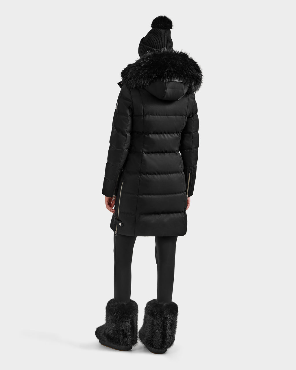 A person stands facing away, wearing the Rudsak KEHLANI H - 8125643 Black women’s down parka with a fur-lined hood—a true winter essential—against a plain white background.