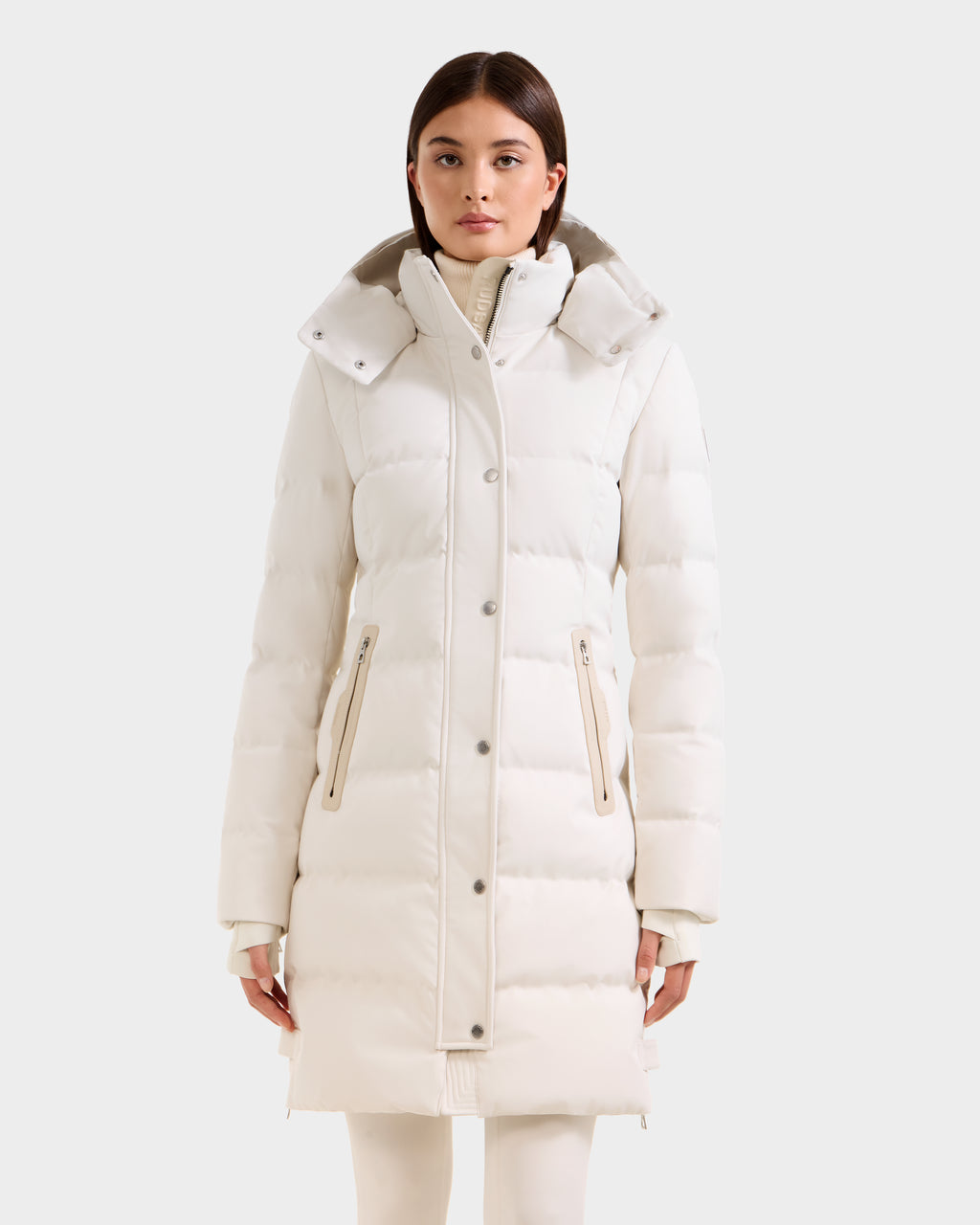 A person wears the Rudsak KEHLANI H - 8125643 Vanilla, a long cream women’s down parka with high collar and zippered pockets, filled with RDS-certified down for warmth and comfort, standing against a plain light background.