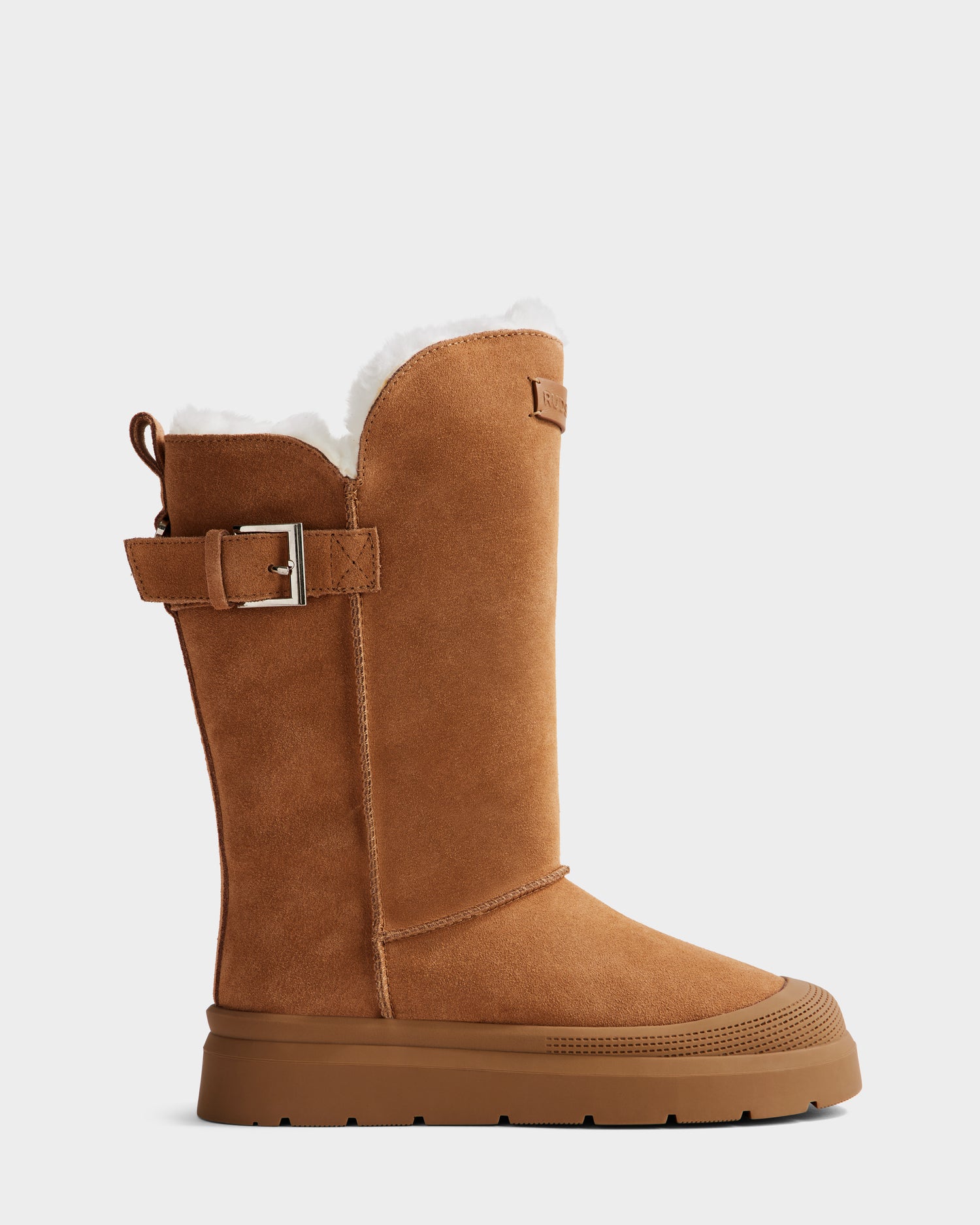 Shown in profile against a plain white background, the Rudsak KLAIR - L225027 Tan is a women's tan suede mid boot featuring a side buckle, white fleece lining, and a thick brown rubber sole.