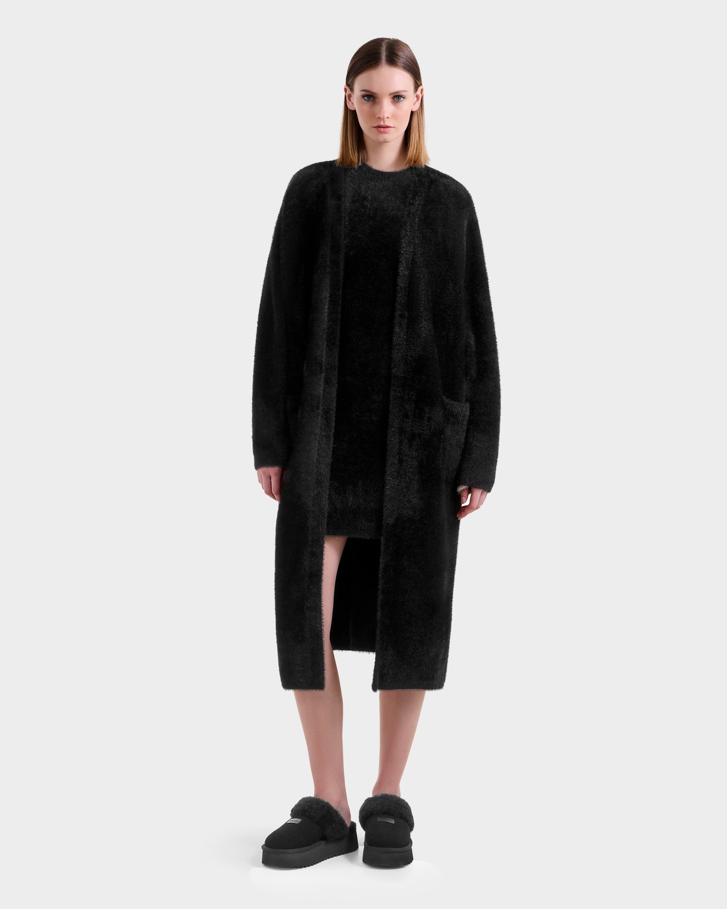 A woman faces forward against a plain white background, wearing the Rudsak LACEY - 8525694 Black fuzzy cardigan layered over a matching black dress and black slip-on shoes.