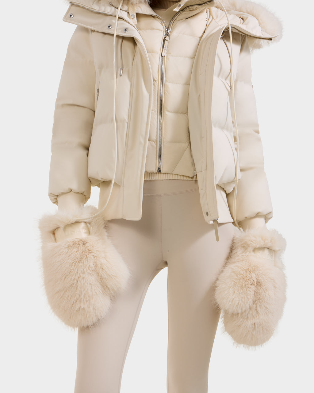 A person wears the Rudsak LIRA - 8425024 Vanilla puffer jacket with matching fitted pants and oversized faux fur mittens—all in soft neutral tones. This cozy outfit from Rudsak delivers stylish winter warmth, perfect for chilly days.