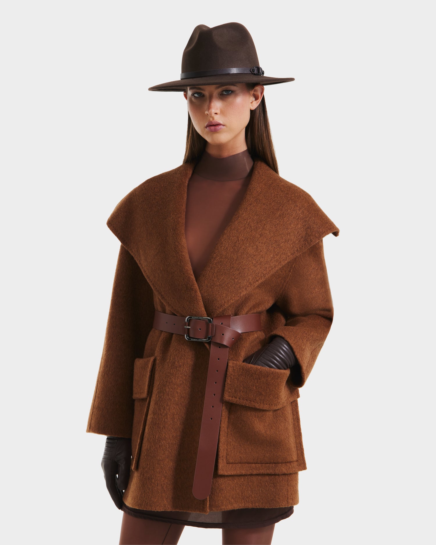 A woman wearing the Rudsak LUCIA - 8125633 Camel women’s wool jacket with a vegan leather belt and large lapels stands against a plain white background.