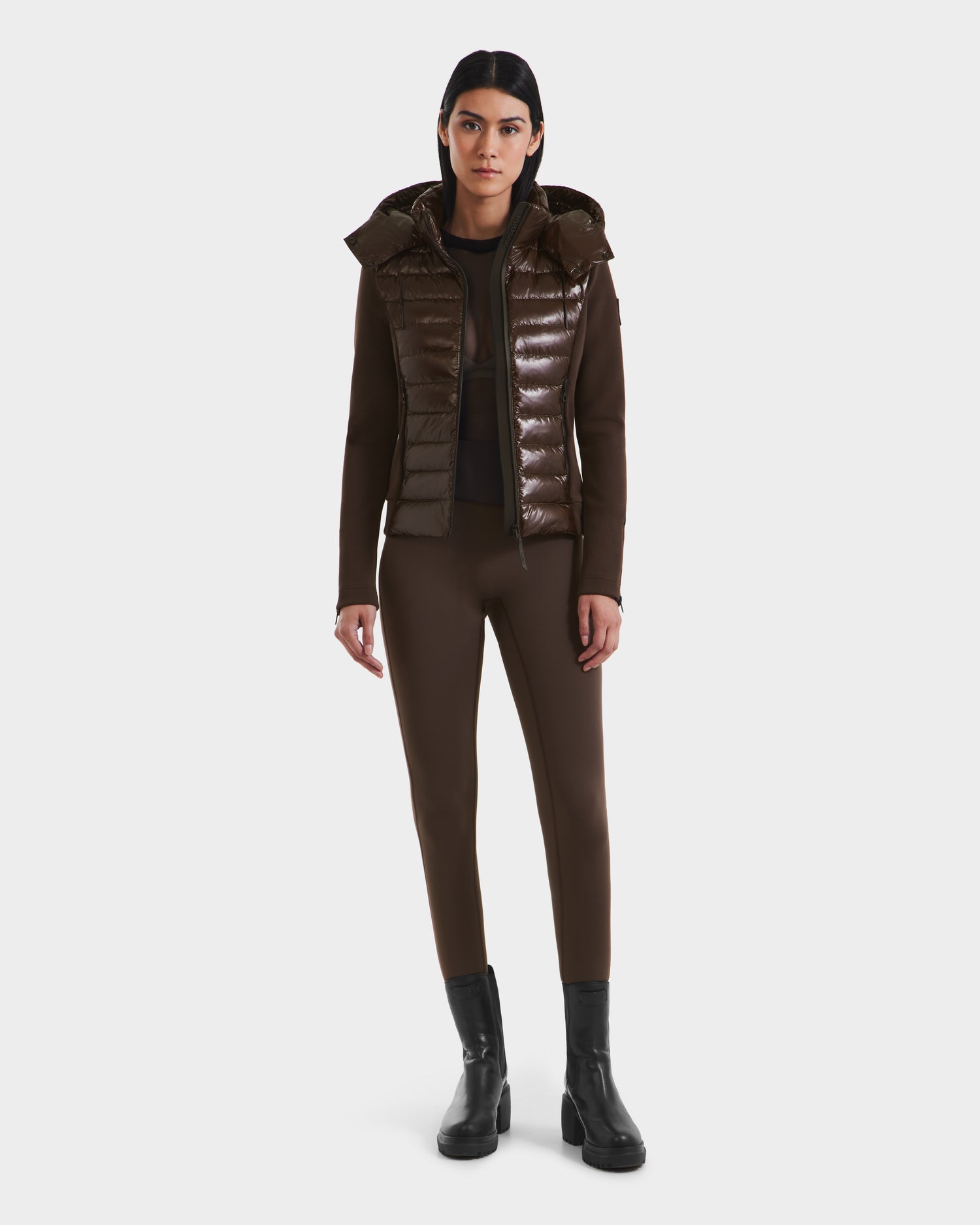 A person faces forward wearing the Rudsak MABS C - 8124590 Espresso women’s shiny brown puffer jacket with a hood, paired with matching brown fitted pants and black ankle boots against a plain white background.