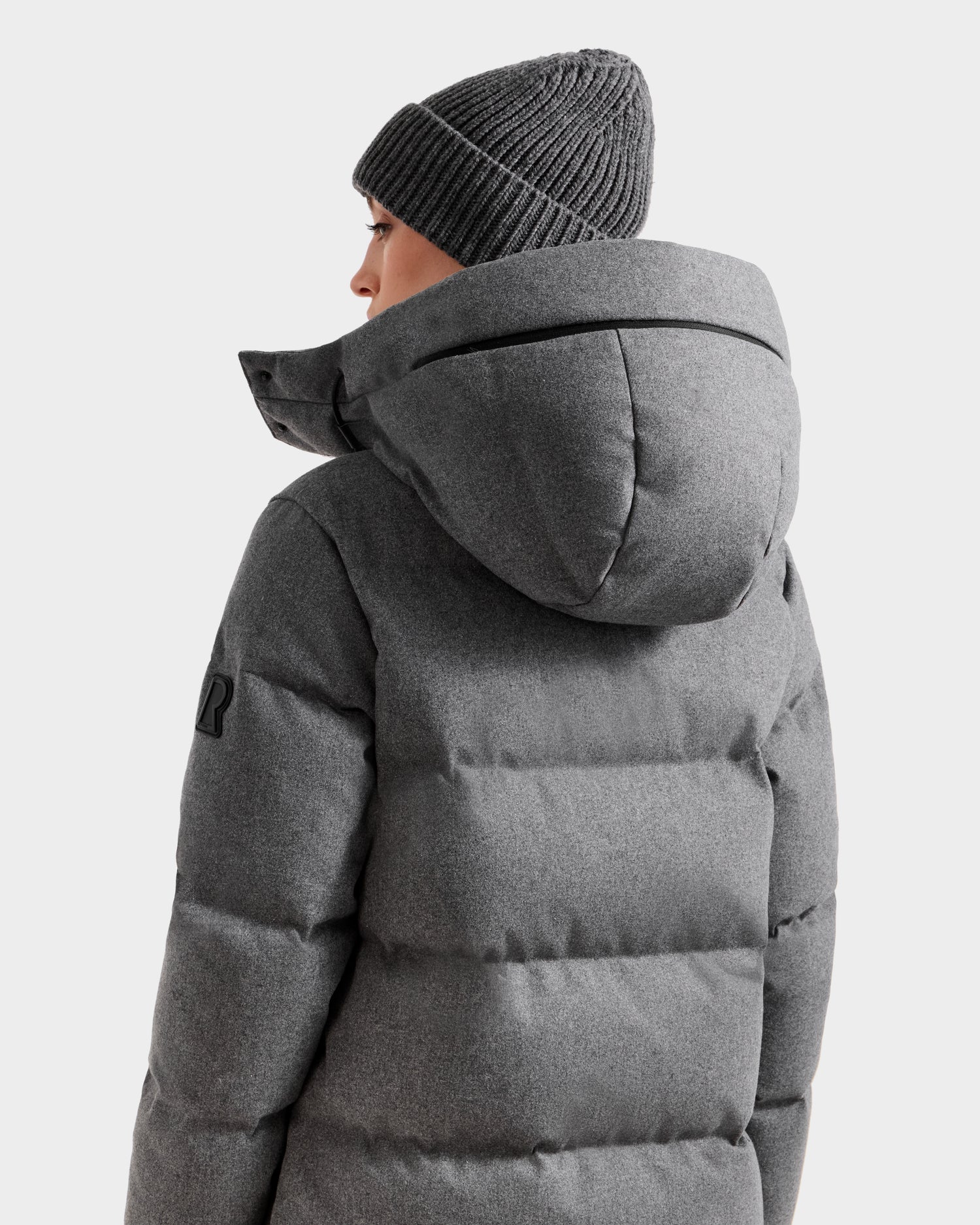 A person in the Rudsak MAO W - 8125568 Heather Charcoal puffer coat and a wool-blend shell beanie, both in grey, is shown from the back against a plain light background—perfect for winter outerwear.