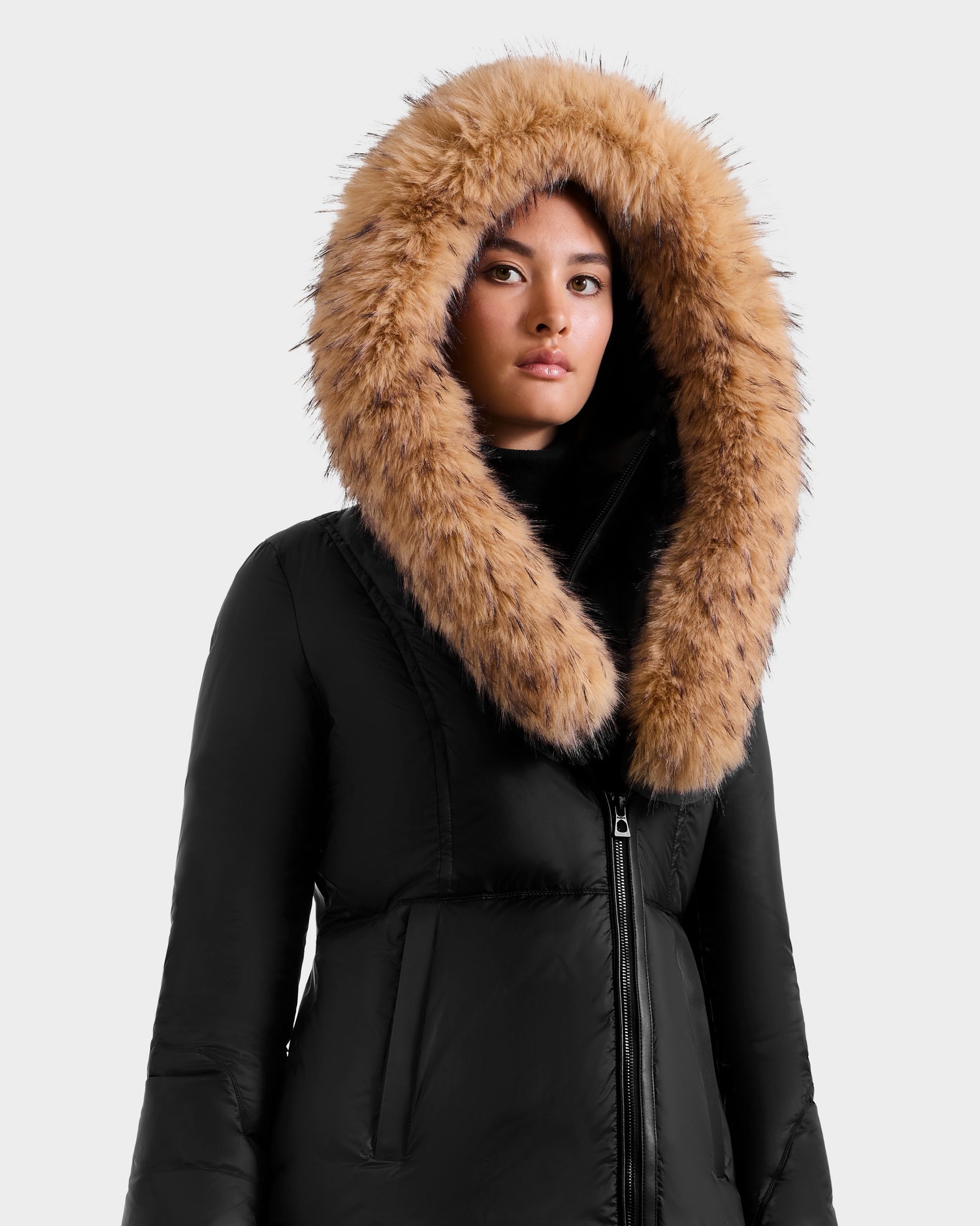 A woman wears the Rudsak MARTINA FF - L125609 Black puffer jacket with RDS-certified down fill and a large removable faux fur hood border, standing against a plain light background and looking at the camera.