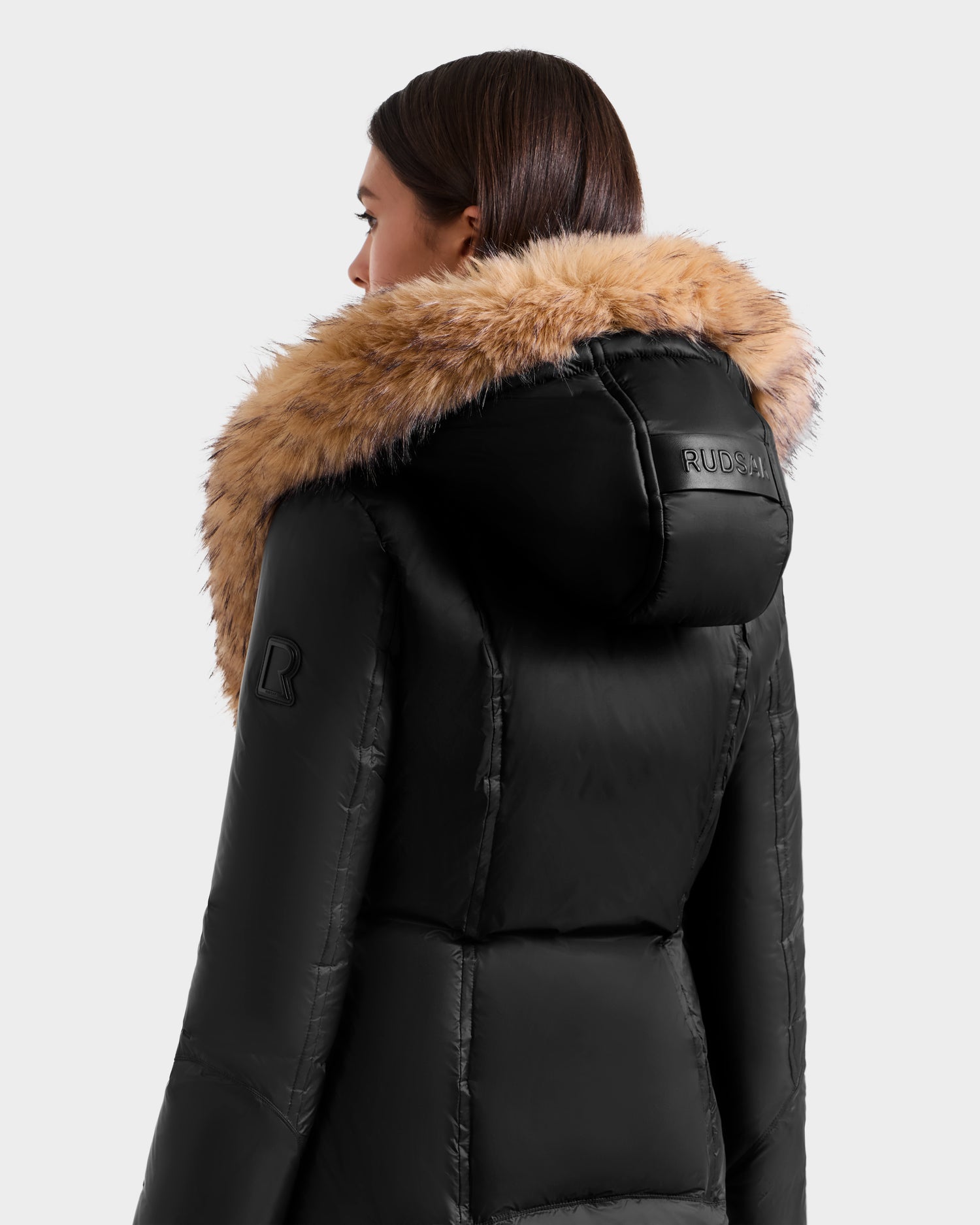A woman wears the MARTINA FF - L125609 Black mid-length puffer coat by Rudsak, featuring a hood with a removable faux fur trim.