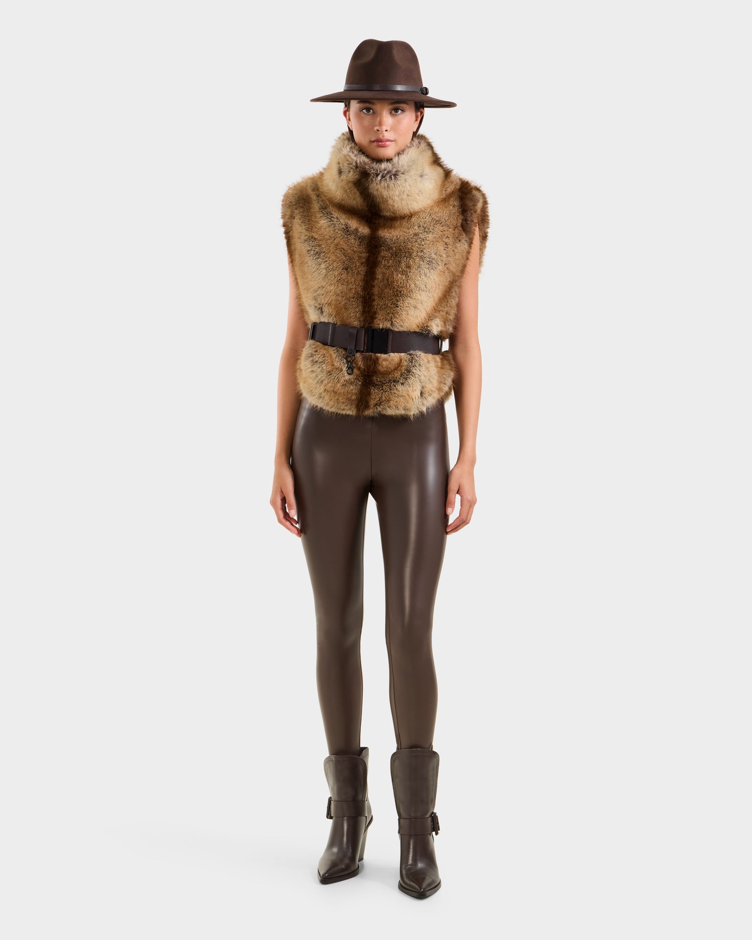 A person models the Rudsak MAULIN - 8524611 Mix Mocha sleeveless faux fur vest, paired with a brown hat, fitted pants, and boots against a white background, highlighting chic layering style.
