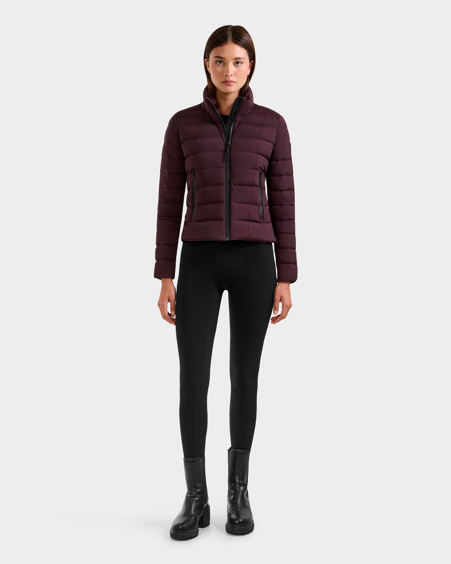 A woman faces forward against a plain white background, wearing the Rudsak MELISSA - 8125054 Bordeaux RDS certified down puffer jacket, black fitted pants, and black ankle boots.