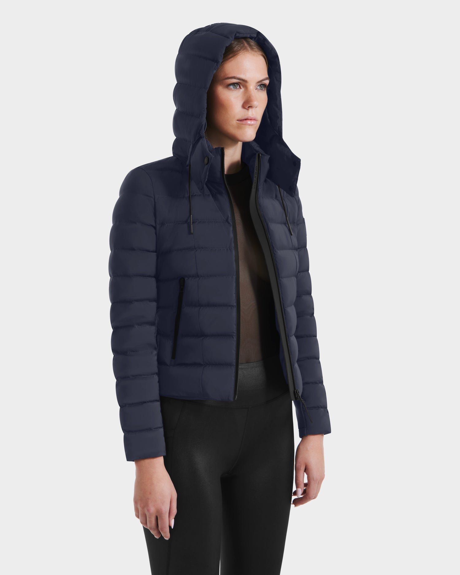 A person wears the Rudsak MELISSA - 8125054 Navy women’s puffer jacket with RDS certified down over a dark top and black pants, standing slightly turned against a plain white background.