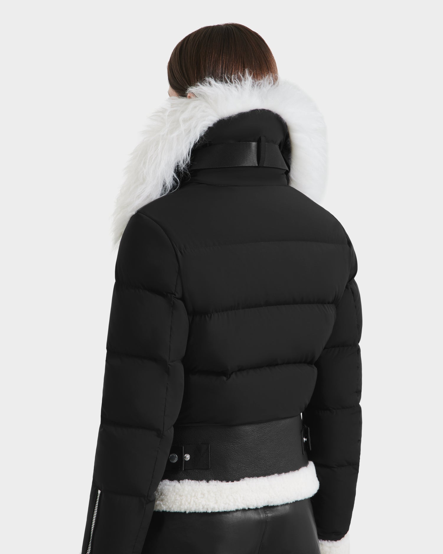 A person with straight brown hair, seen from behind, wears the Rudsak MONKA - 8125629 Black women’s shearling jacket with a Mongolian shearling collar and leather waist and cuff details against a plain, light background.