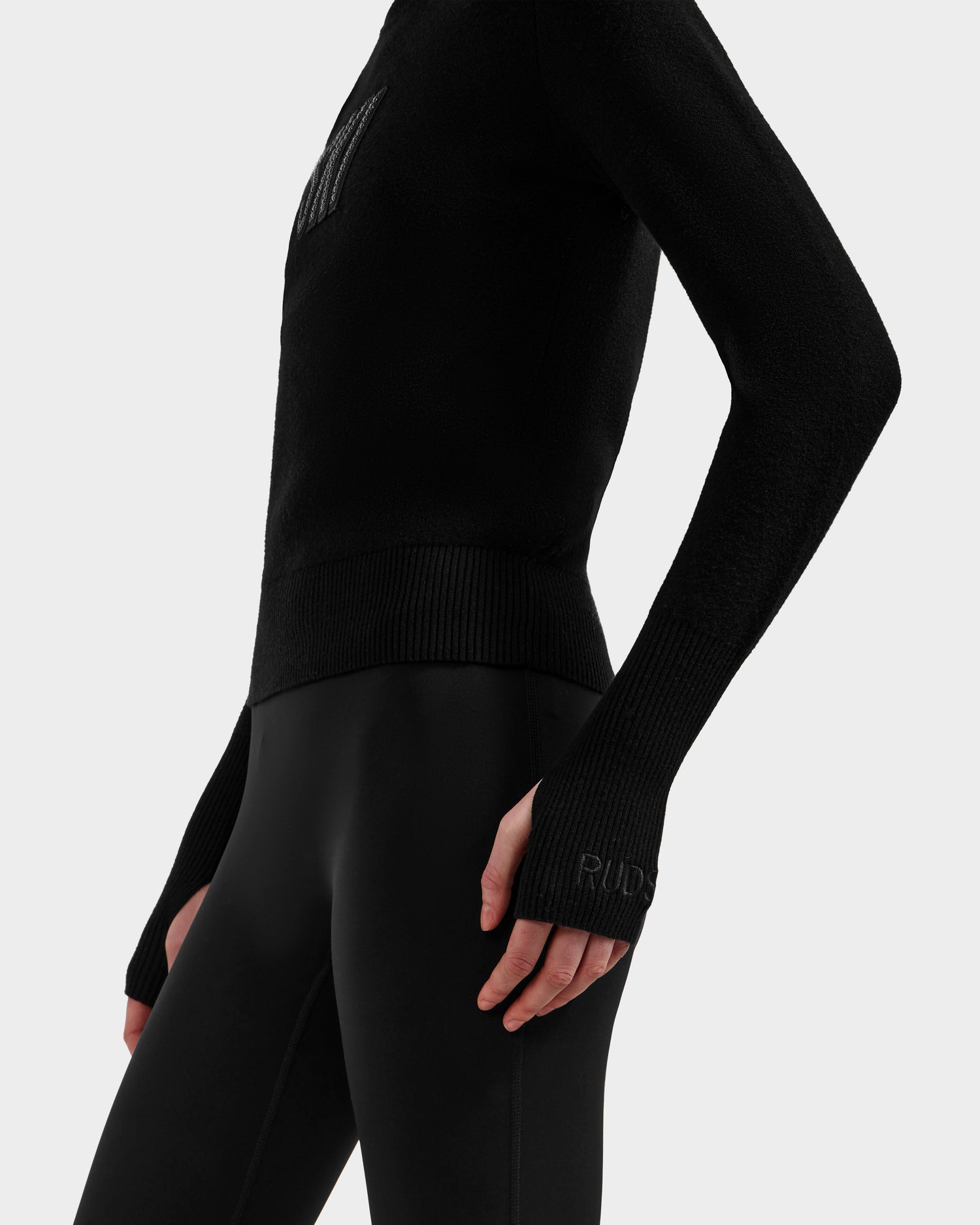A person wearing the Rudsak NOVIE - 8525659 Black fitted après-ski sweater and black leggings, shown from the waist up in a side view with one hand by their thigh against a plain light background.