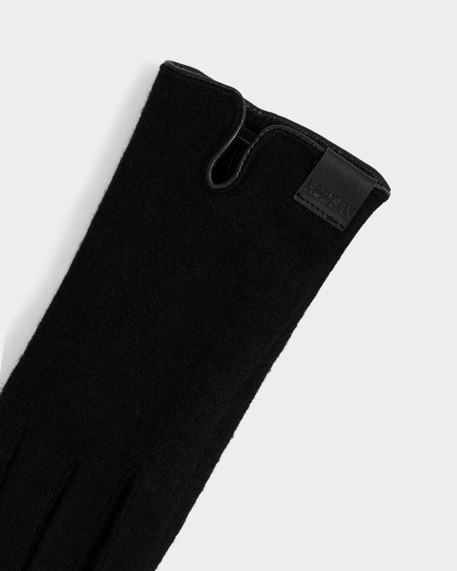 A close-up of the OLGA - L425541 Black women's wool glove, a cold-weather essential with soft texture and subtle seams, featuring a small leather tag near the cuff embossed with the Rudsak brand name in uppercase letters.