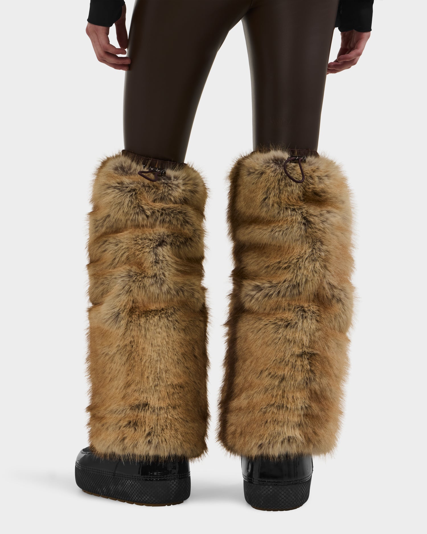 A person models the Rudsak PAIGE - 8425534 Mix Mocha brown faux fur leg warmers over black platform shoes and dark brown pants, shown from the back against a plain white background.