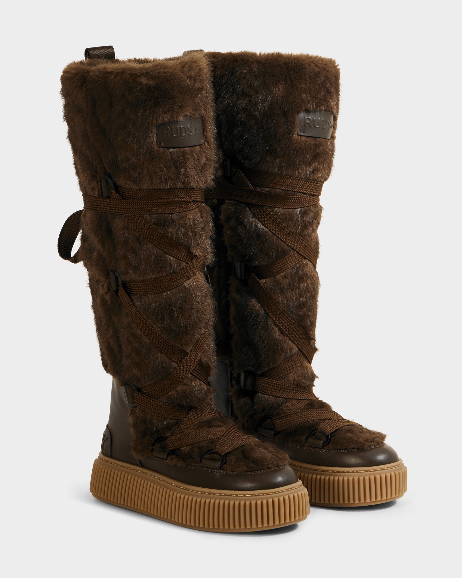 The Rudsak PALERMO C - 8225546 Mocha are knee-high women’s faux fur winter boots in brown with dark brown crisscross laces, black leather accents, and thick ribbed tan soles—ideal for après-ski style.