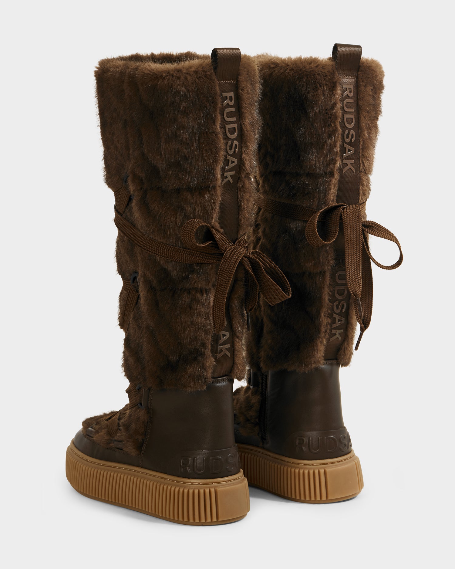 The Rudsak PALERMO C - 8225546 Mocha women's boots feature tall brown faux fur, tan rubber soles, brown back laces, and Rudsak branding—ideal winter footwear for stylish après-ski warmth and comfort.