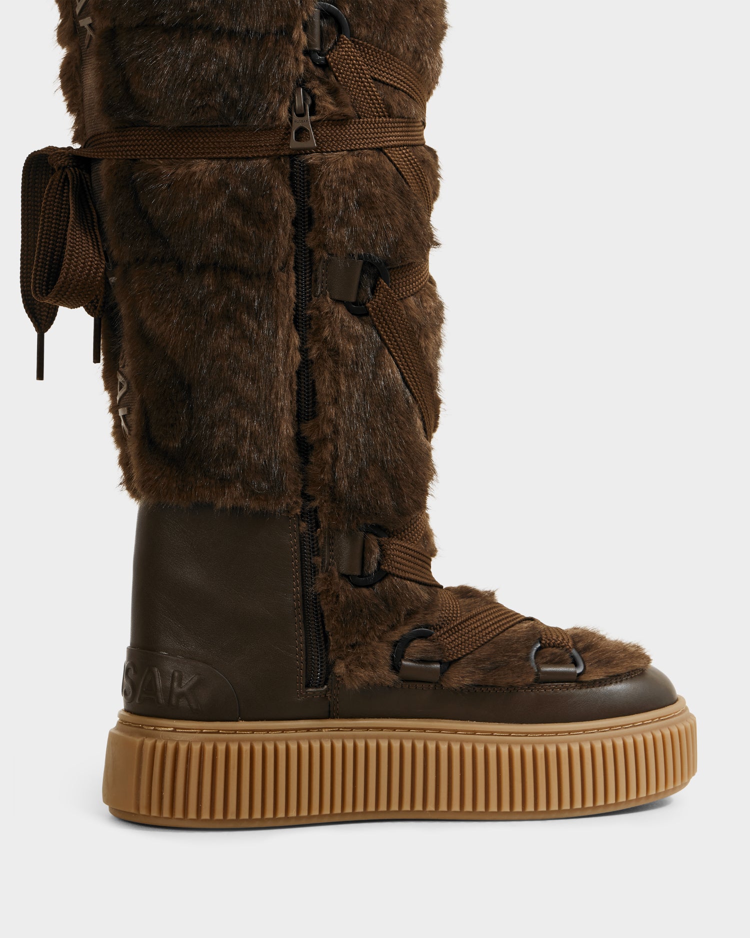 Side view of the Rudsak PALERMO C - 8225546 Mocha, a knee-high women's winter boot in brown with faux fur, leather-like materials, chunky ribbed rubber sole, zipper, and crisscrossing brown laces.