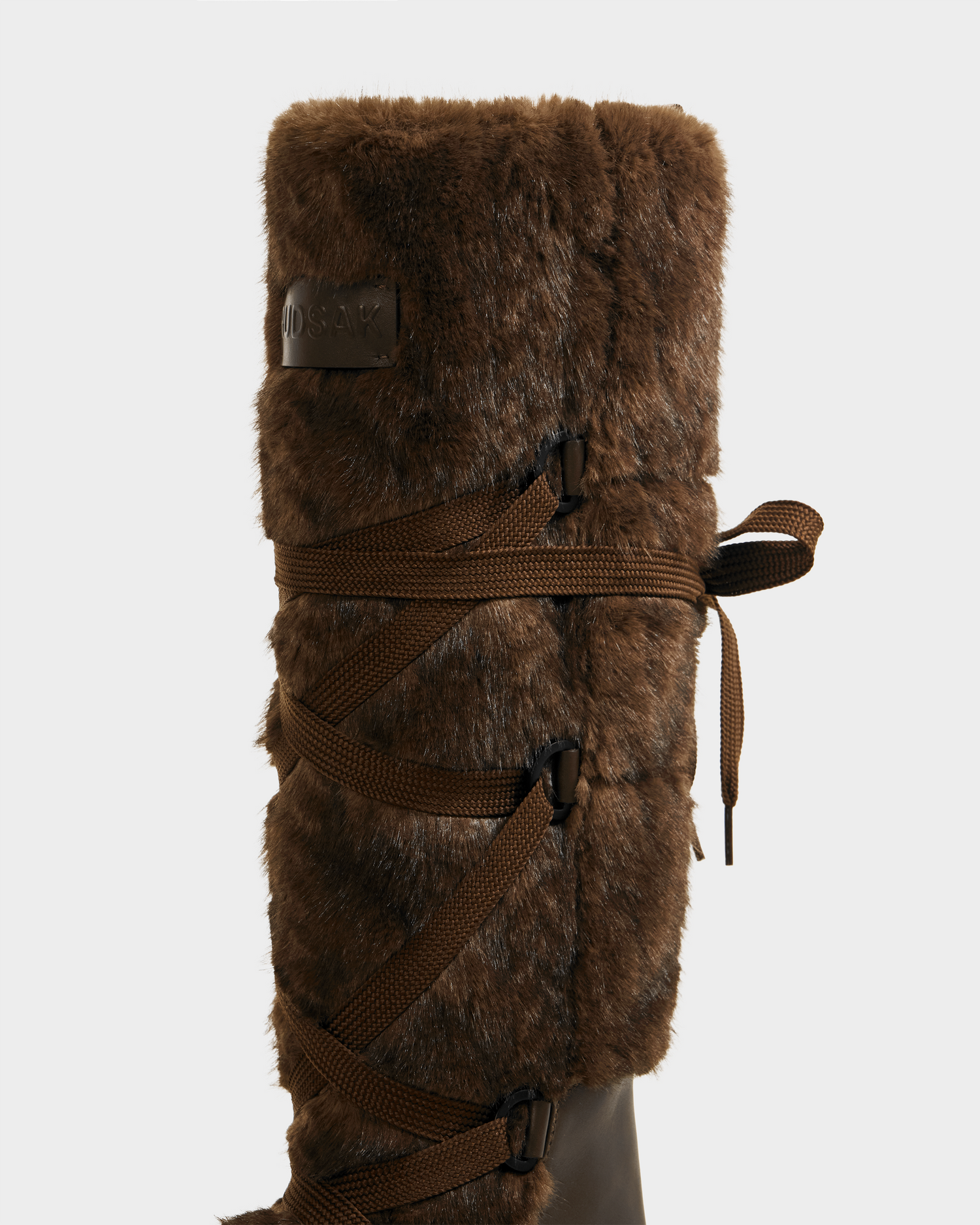 A close-up of the Rudsak PALERMO C - 8225546 Mocha women’s faux fur winter boot with crisscrossed laces and a side bow, set against a light background—ideal for chic, cozy après-ski style.