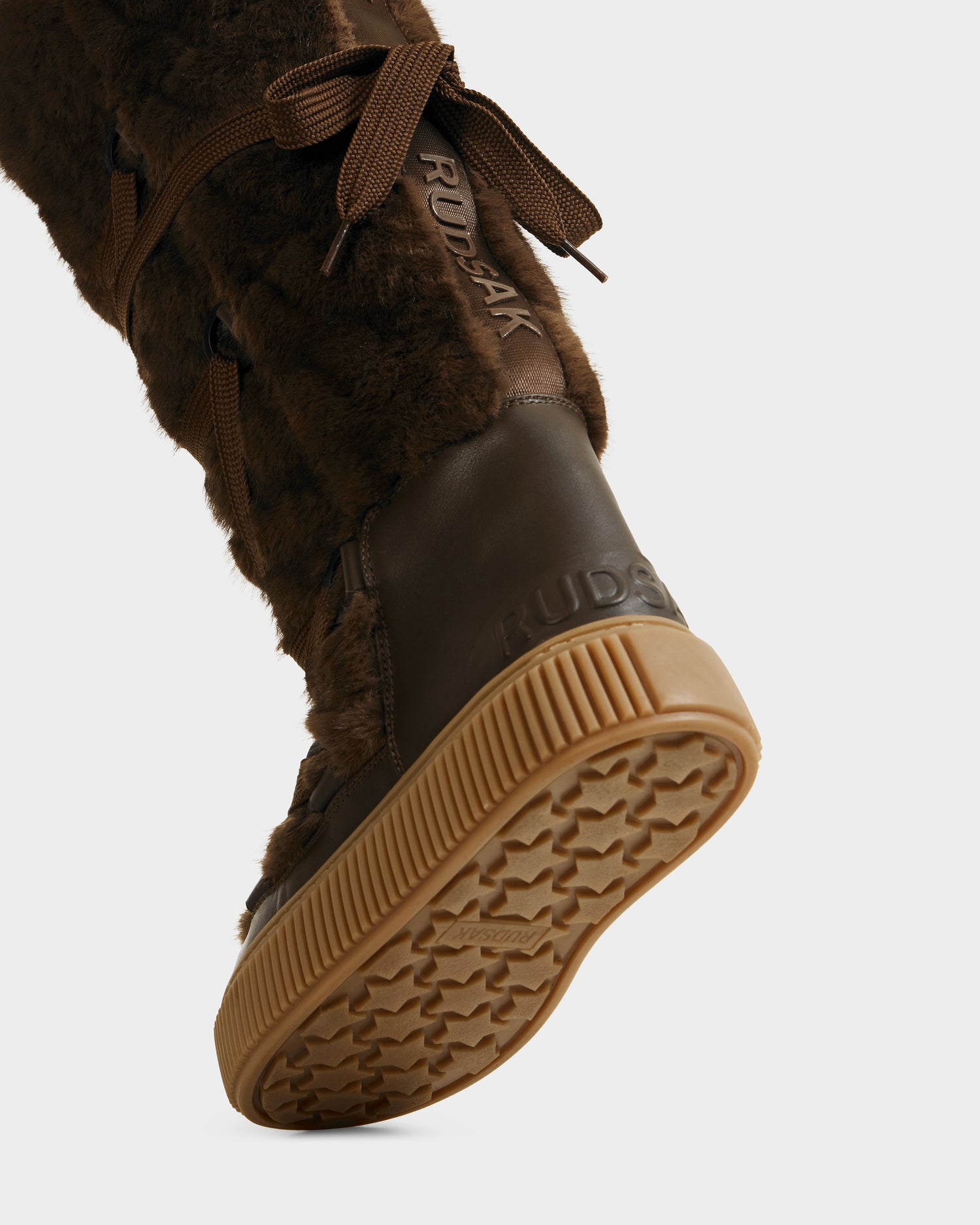 Close-up of the Rudsak PALERMO C - 8225546 Mocha women’s winter boot with faux fur trim, lace-up detail, brand name on side and heel, and a tan rubber sole with star tread. Perfect for cozy après-ski style.