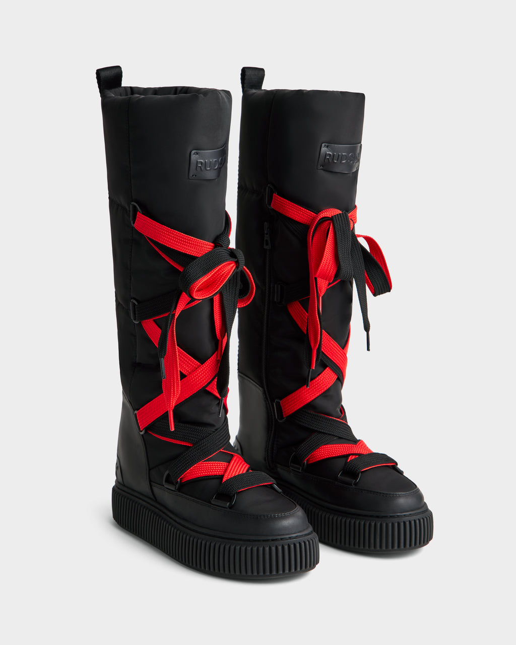 The Rudsak PALERMO - 8225030 Black boots feature tall insulated black uppers, chunky soles, and bold red crisscross laces—stylish women’s winter boots providing warmth against a plain light backdrop.