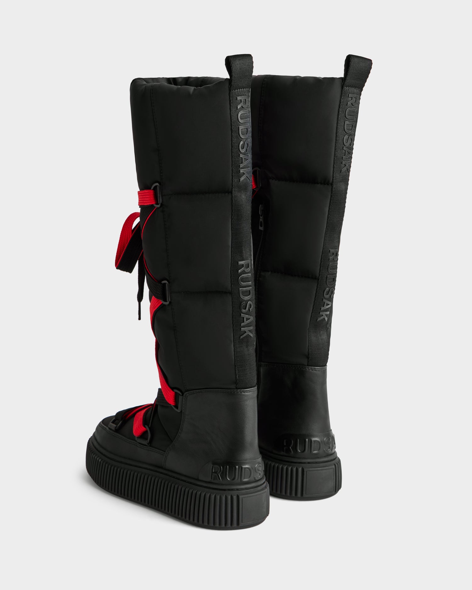 The PALERMO - 8225030 Black women's knee-high boots by Rudsak feature a quilted design, thick soles, bold red laces, and “RUDSAK” branding. These insulated boots keep you warm and stylish all winter.