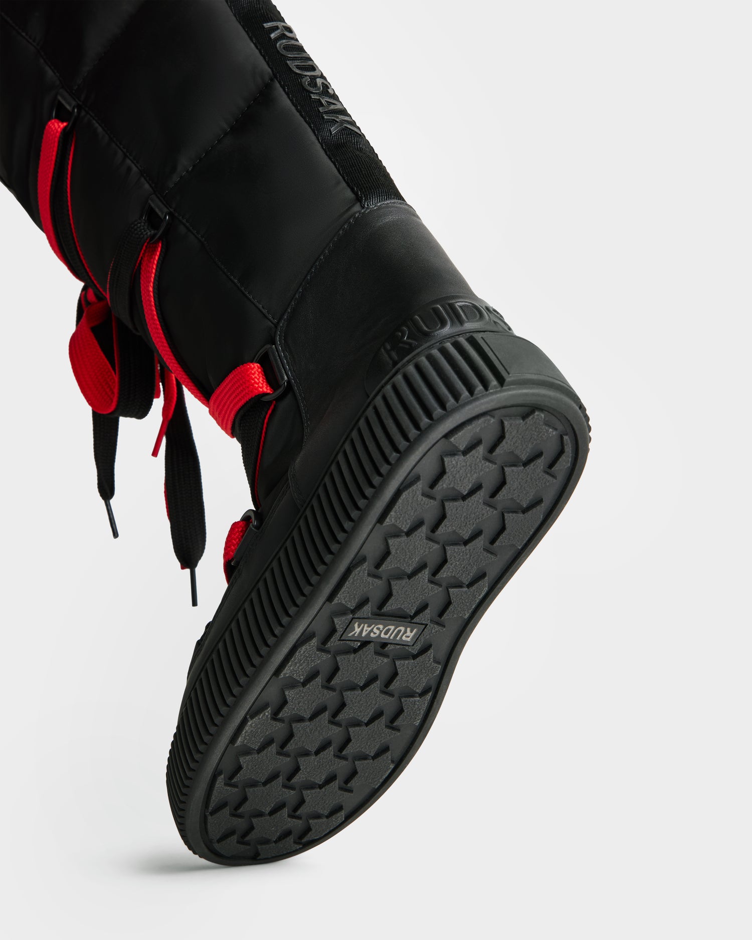 Close-up of the water-resistant sole on Rudsak’s PALERMO - 8225030 Black women’s winter boot. The rugged, star-shaped tread and red laces stand out, with the Rudsak logo shown on both the side and bottom.