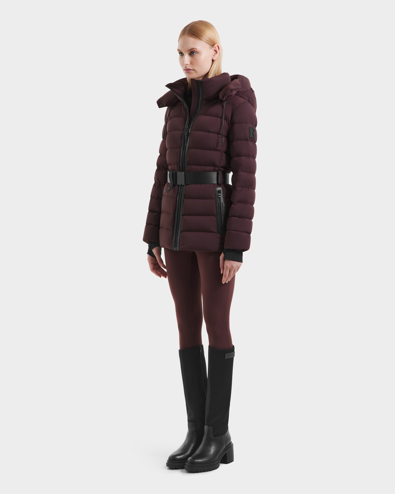 A woman with straight blonde hair models the Rudsak PELIN S - 8124813 Bordeaux womens down puffer jacket with matching leggings and black knee-high boots against a plain white background.