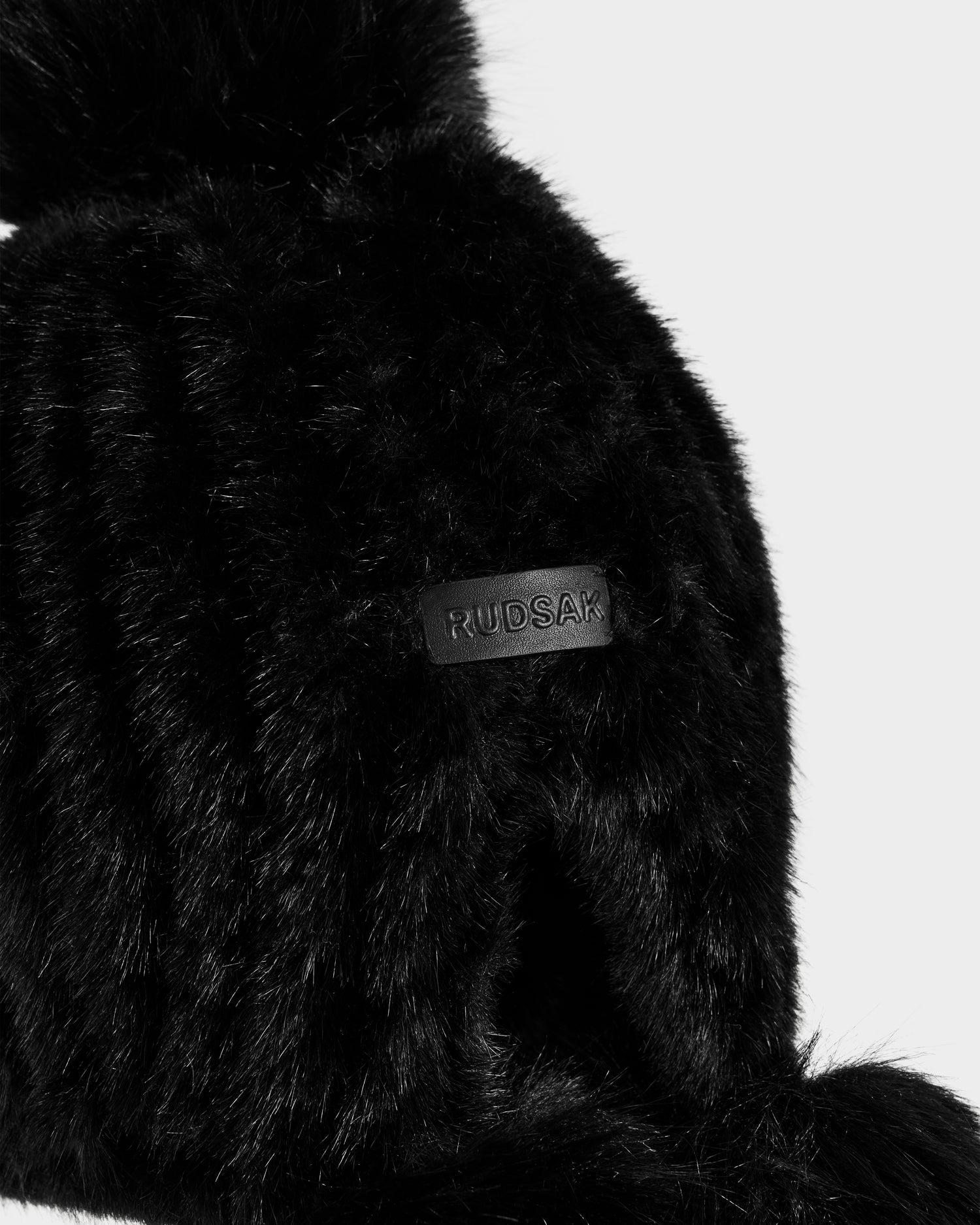 Close-up of the Rudsak PIA - 8425547 Black women’s faux fur hat with a leather patch label, set against a plain light background—an elegant winter accessory.