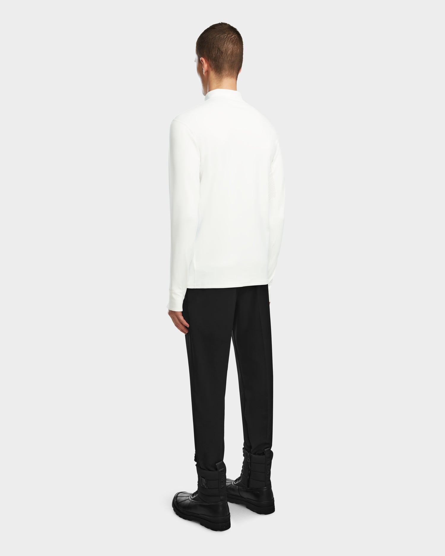 A person faces away, wearing the Rudsak RALI - 6524522 Optic White men’s long-sleeve top as a layering shirt, paired with black pants and boots, set against a plain light background.