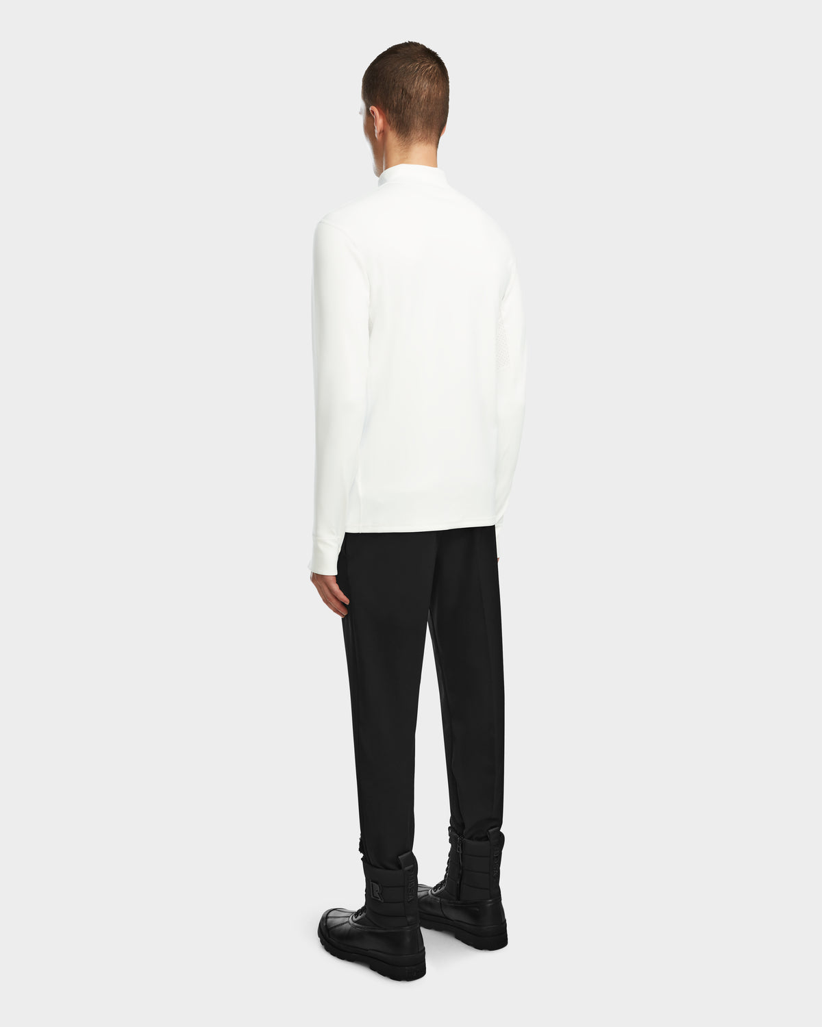 A person faces away, wearing the Rudsak RALI - 6524522 Optic White men’s long-sleeve top as a layering shirt, paired with black pants and boots, set against a plain light background.