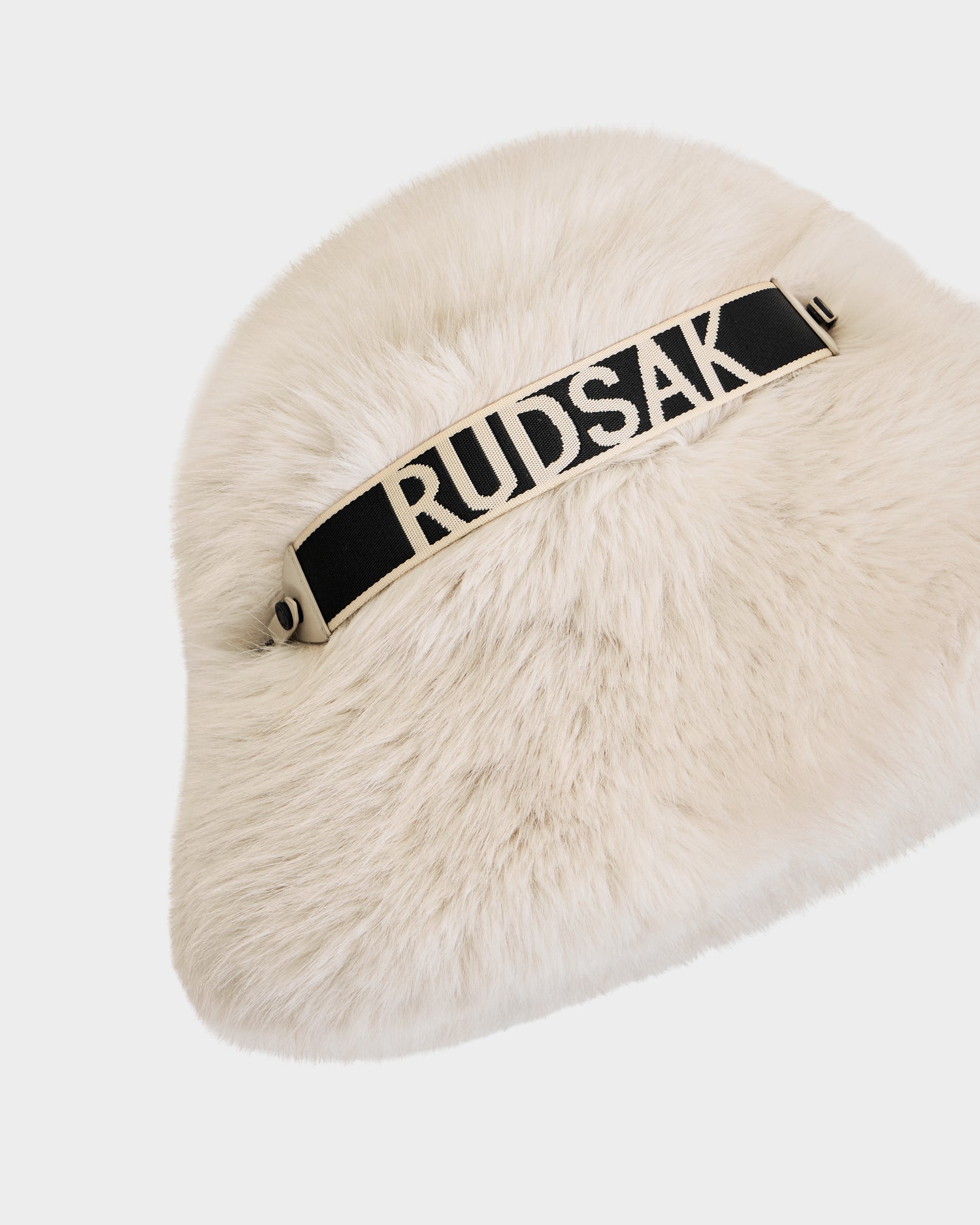 The Rudsak ROMINA - 8425545 Vanilla is a white faux fur bucket hat with a black strap featuring bold white RUDSAK lettering—an ultra-cozy, luxe women’s winter accessory shown on a plain white background.