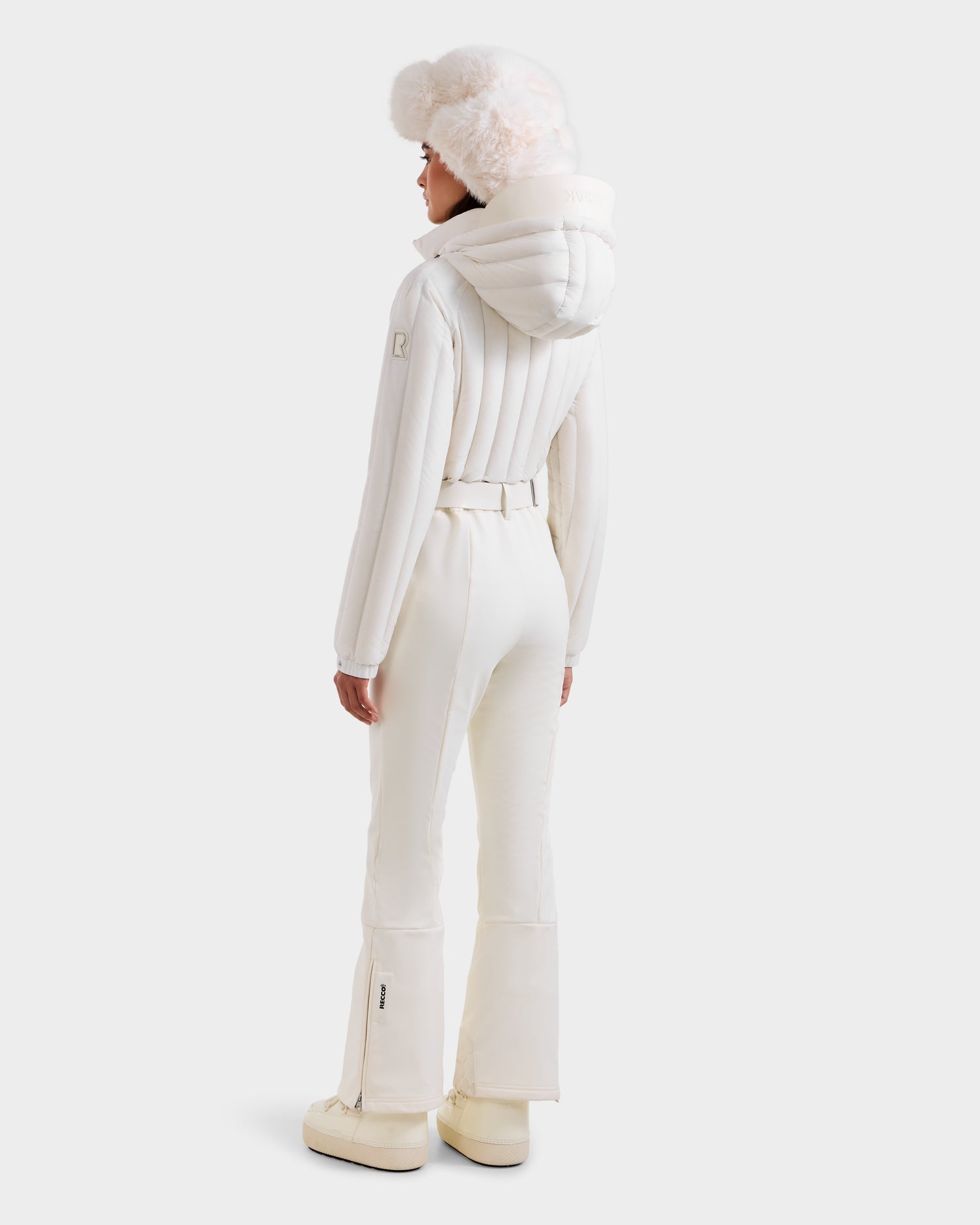 A person faces away in the Rudsak SAGE - 8124782 Iceland women's ski suit—puffy jacket, belted pants, fur hat, and boots—against a plain white background.