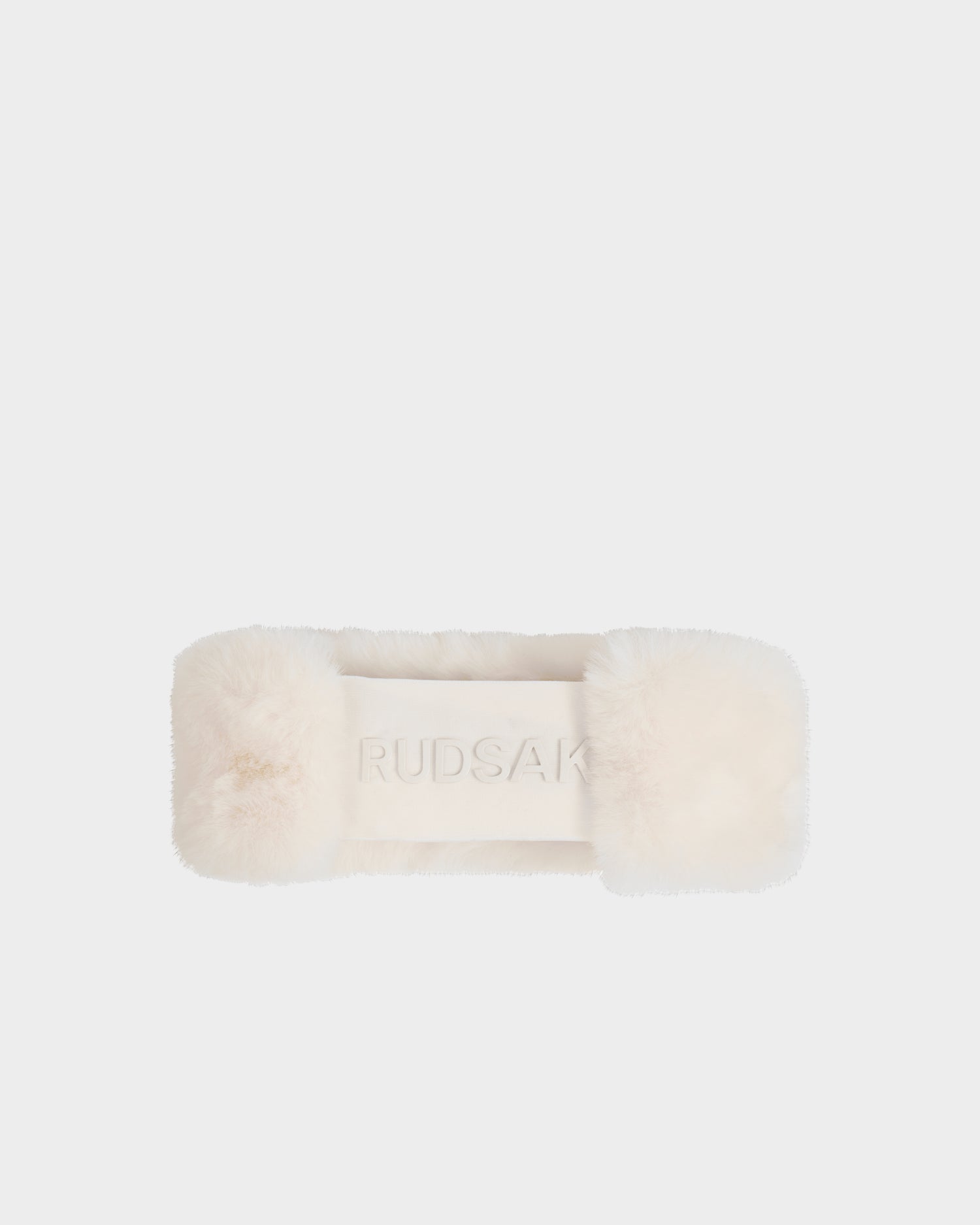 The SANDIE - L425552 Iceland by Rudsak is a cream faux fur women's headband with "RUDSAK" embroidered on the front, shown on a white background—a cozy winter accessory for cold days.