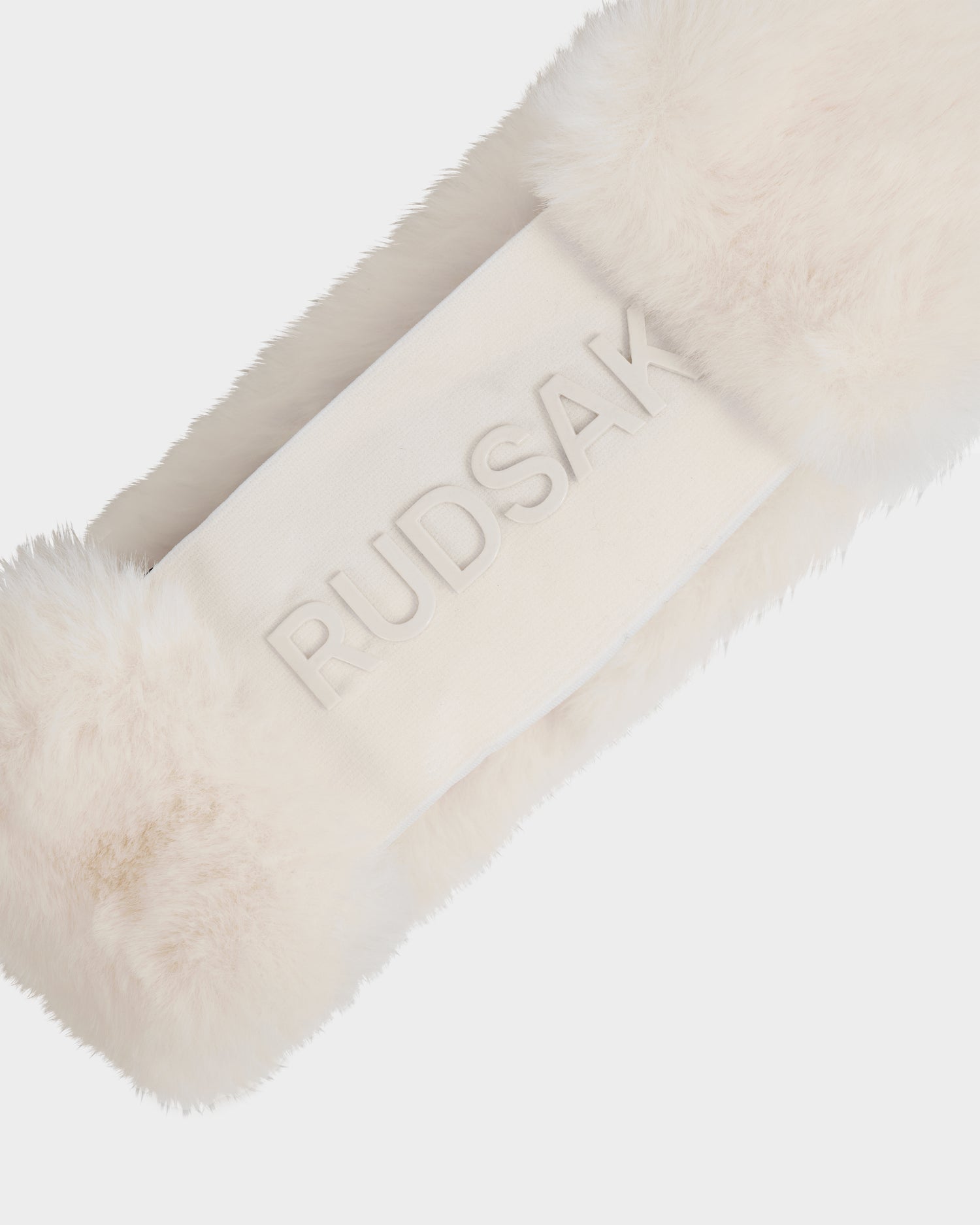 A close-up of the SANDIE - L425552 Iceland white faux fur headband by Rudsak for women, featuring a smooth band embossed with the brand name. This soft, luxurious winter accessory is shown against a plain white background.
