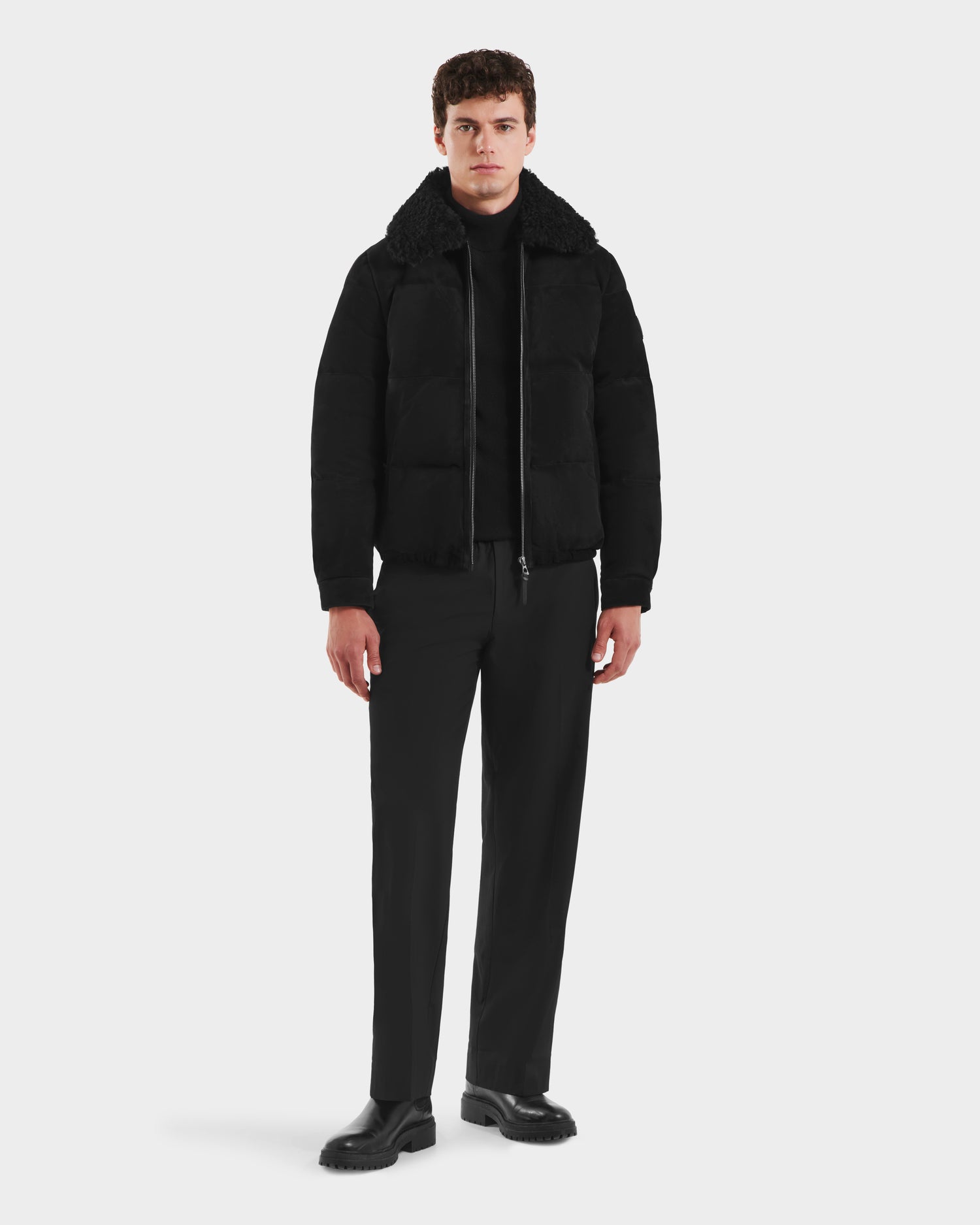 A man faces forward against a white background, wearing the Rudsak SCOTT - 6125685 Black men’s aviator bomber jacket with a shearling collar, paired with a black turtleneck, pants, and shoes.