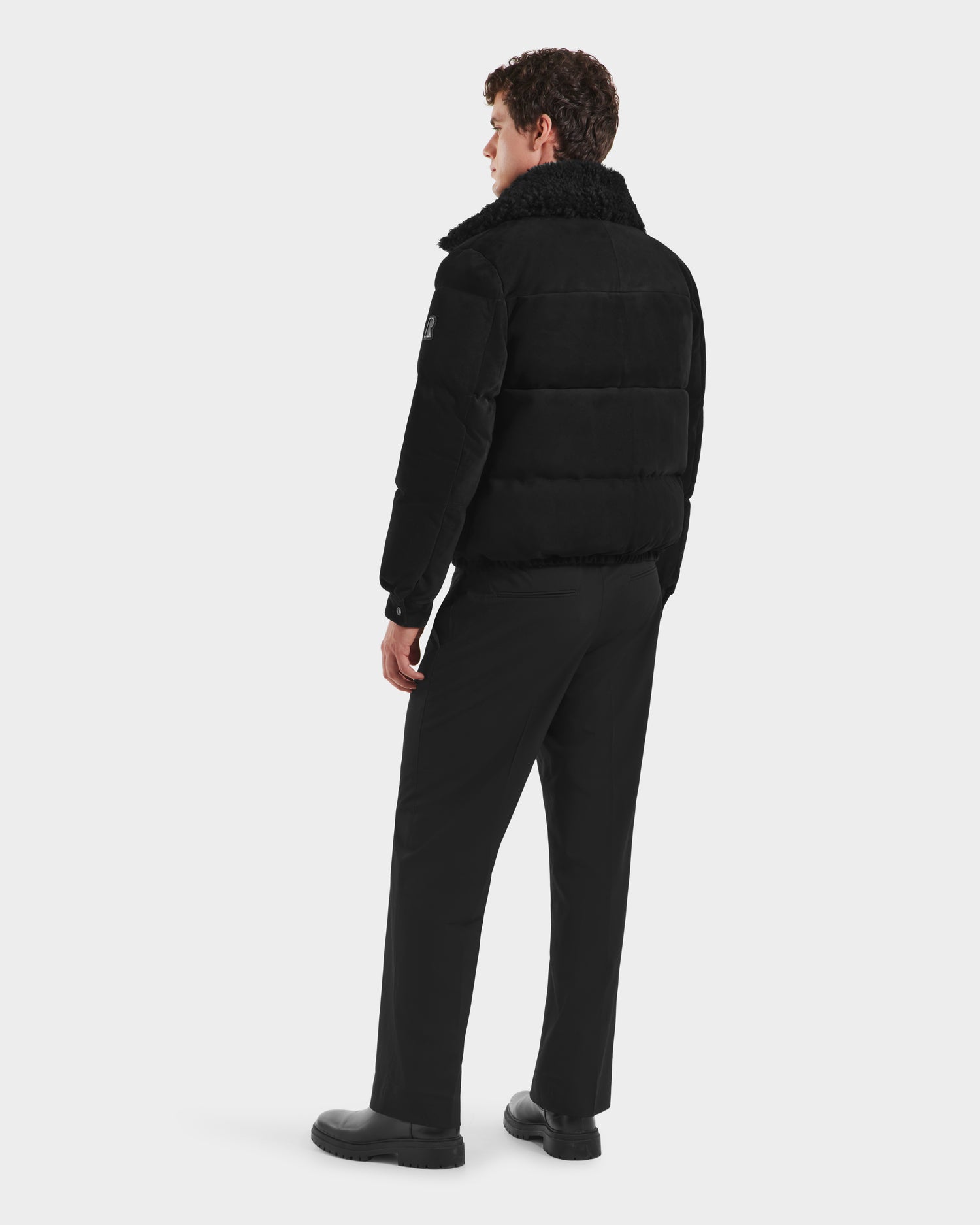 A person stands facing away, wearing the Rudsak SCOTT - 6125685 Black men’s aviator bomber jacket with a shearling collar, paired with black pants and shoes against a plain white background.